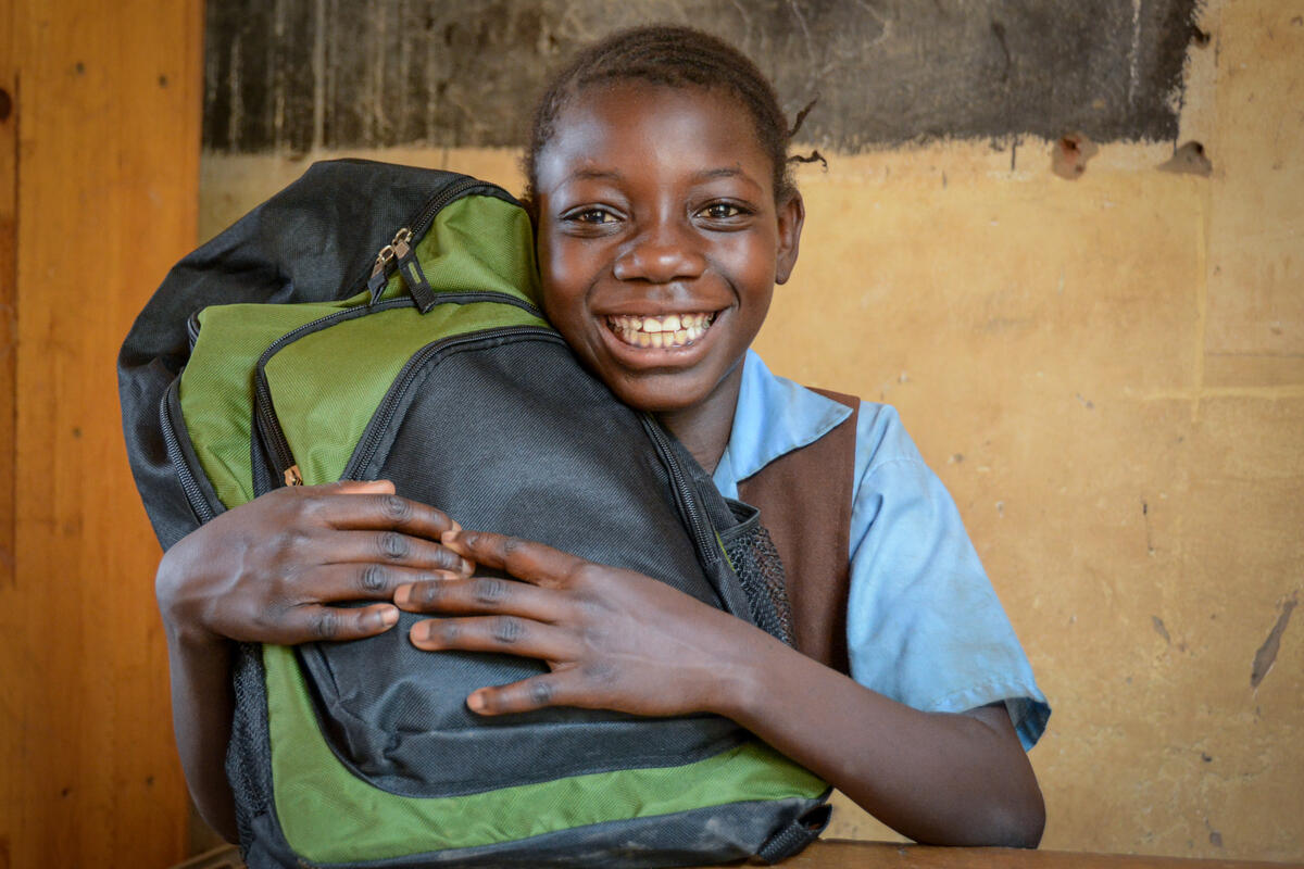 Girl from Zambia smiles to the camera holding her school bag in her arms