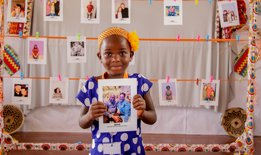 Little girl from Zambia looks to the camera while holding a photo of the sponsors she has chosen