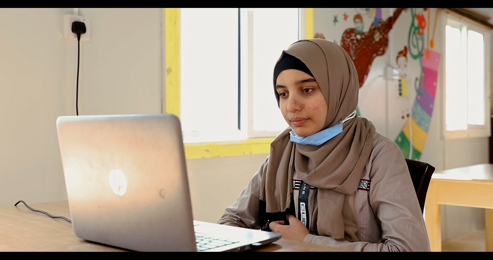 Syrian girl sits in front of a laptop, about to have a zoom call with a teen from the UK