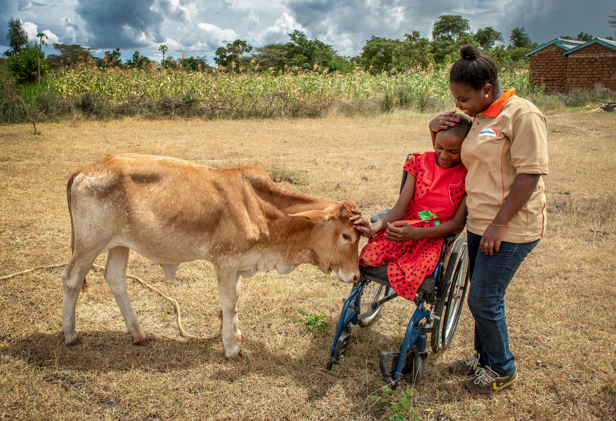 World Vision staff member helps a young girl in a wheelchair to take care of her family's cow