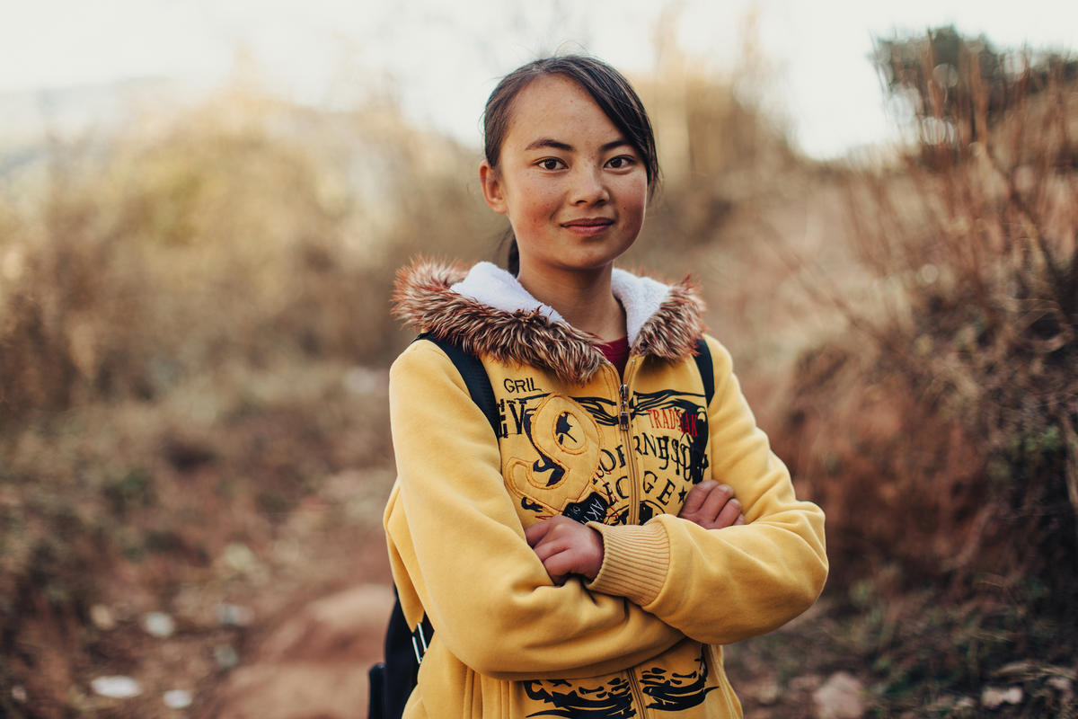 Girl in China smiles at camera in field wearing a backpack