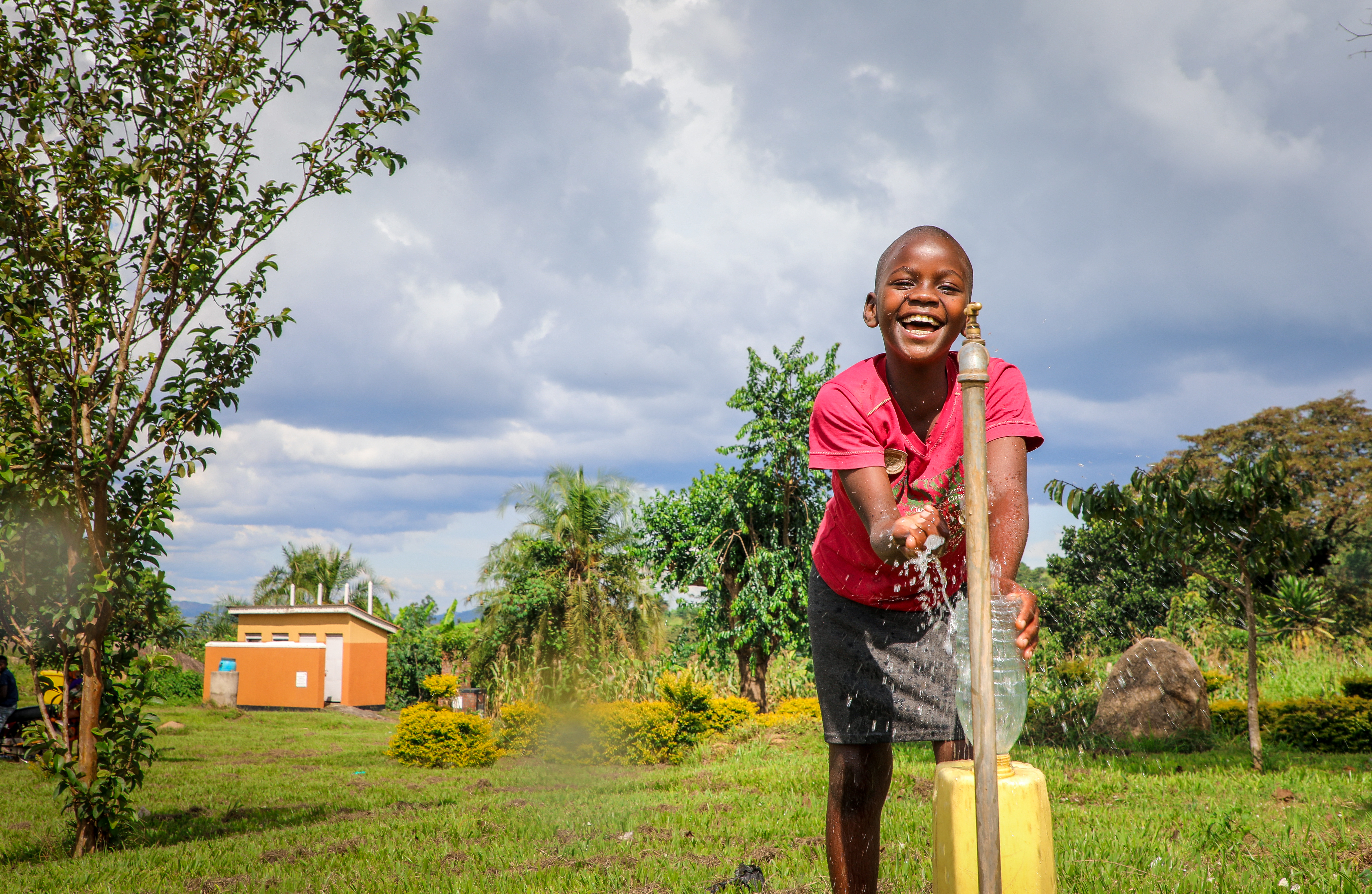 A girl in Uganda smiles while running clean water from a newly-installed tap