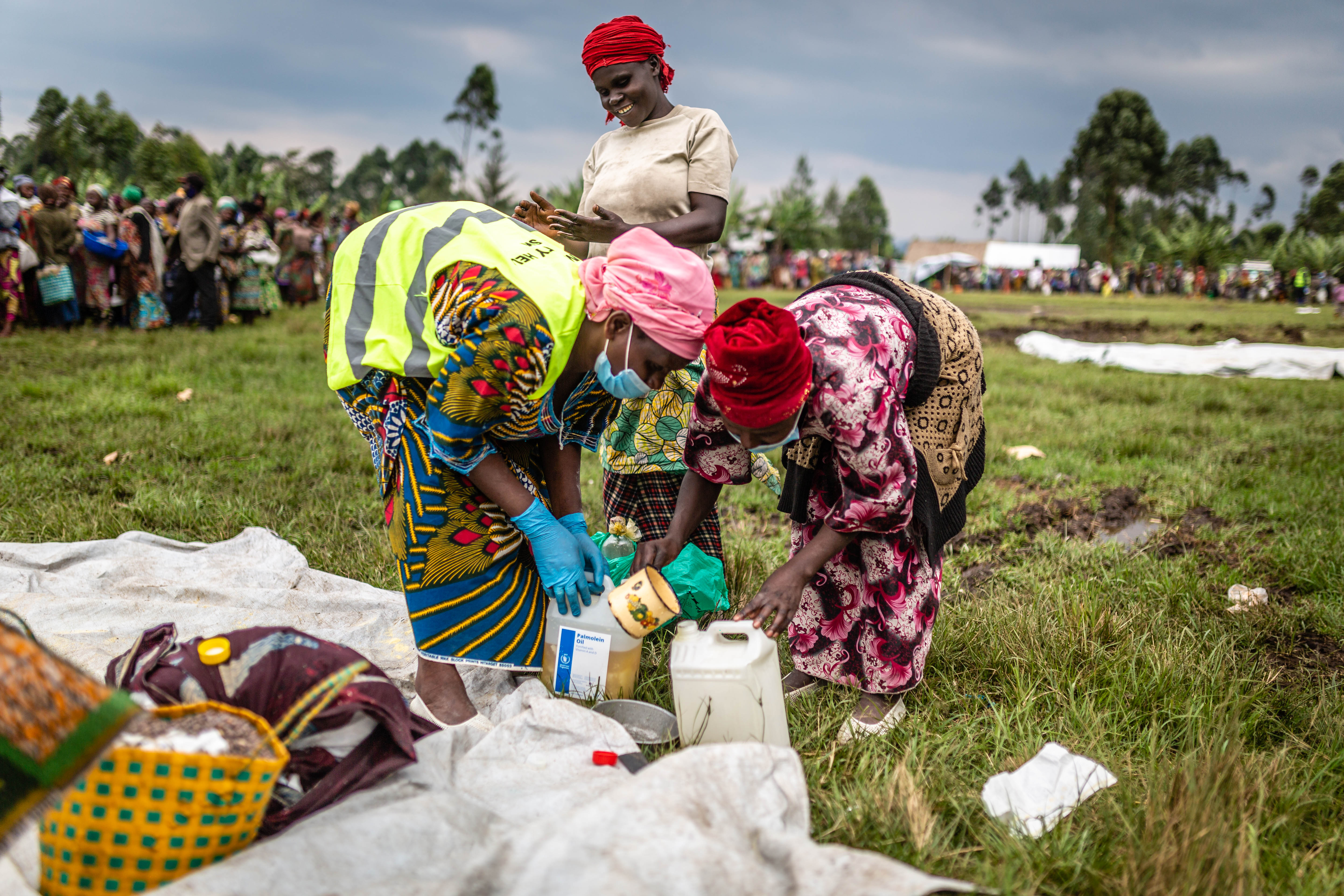 Three women collecting food in the DRC as other wait in the background for their turn filling up containers and bags.