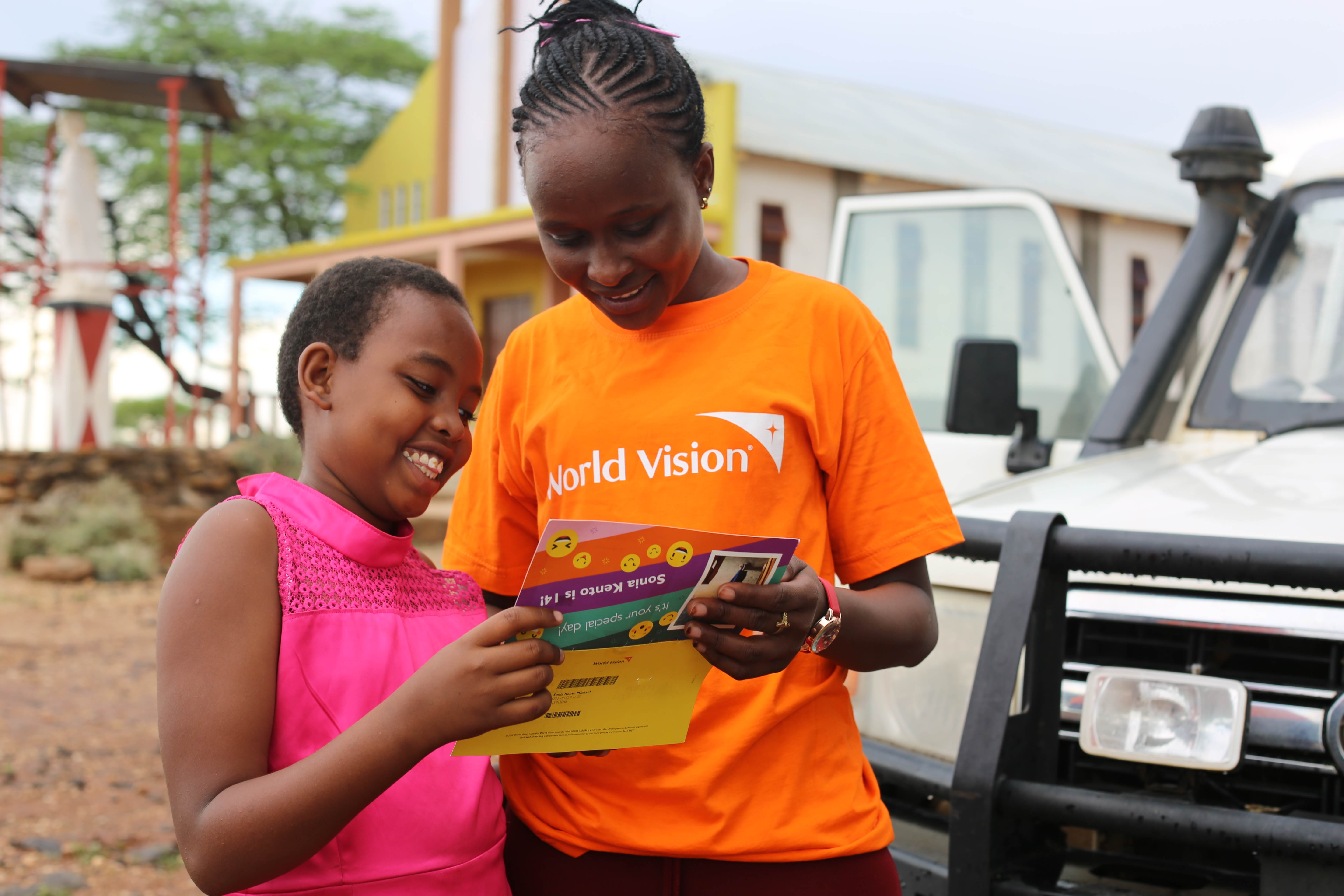 14 year old girl in Kenya, standing next to a World Vision worker, opens post from her sponsor