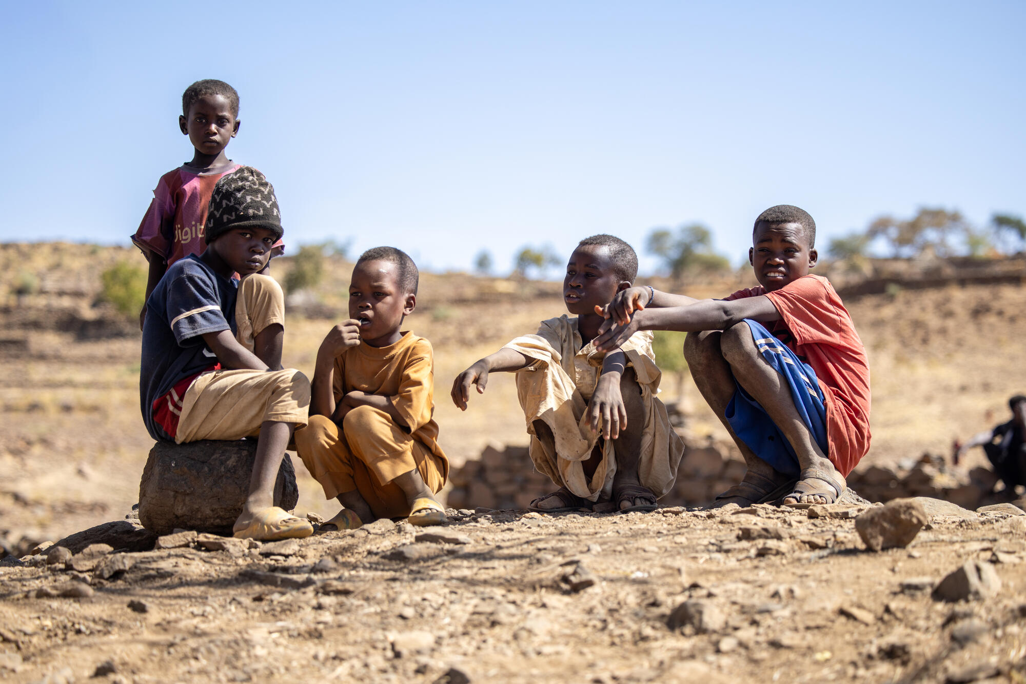 Five children displaced by fighting in Sudan sit on rocky ground looking to the camera
