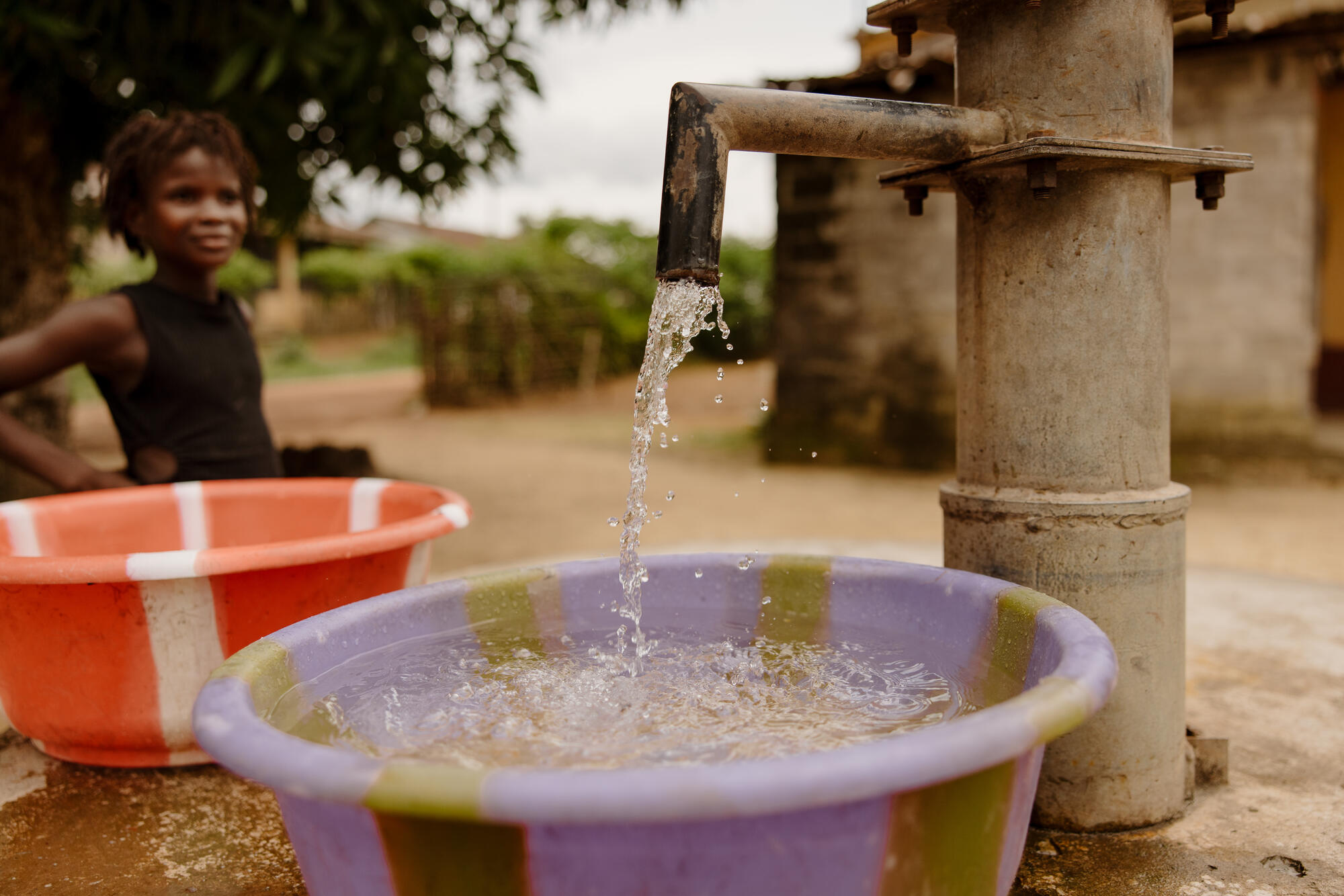 A girl watches water fill a basin at a newly installed tap.
