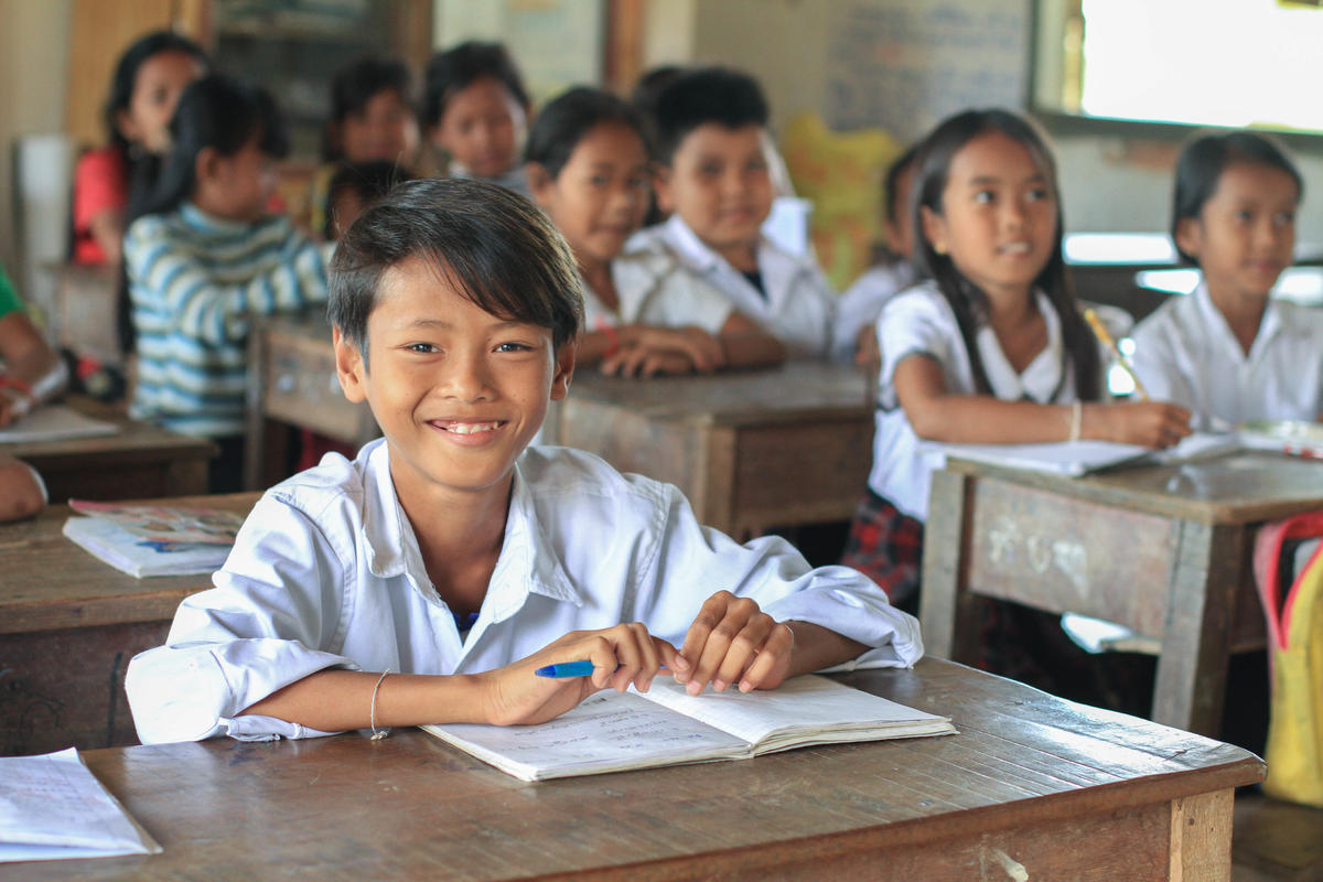 Children in Cambodia sit at their desks and smile over books