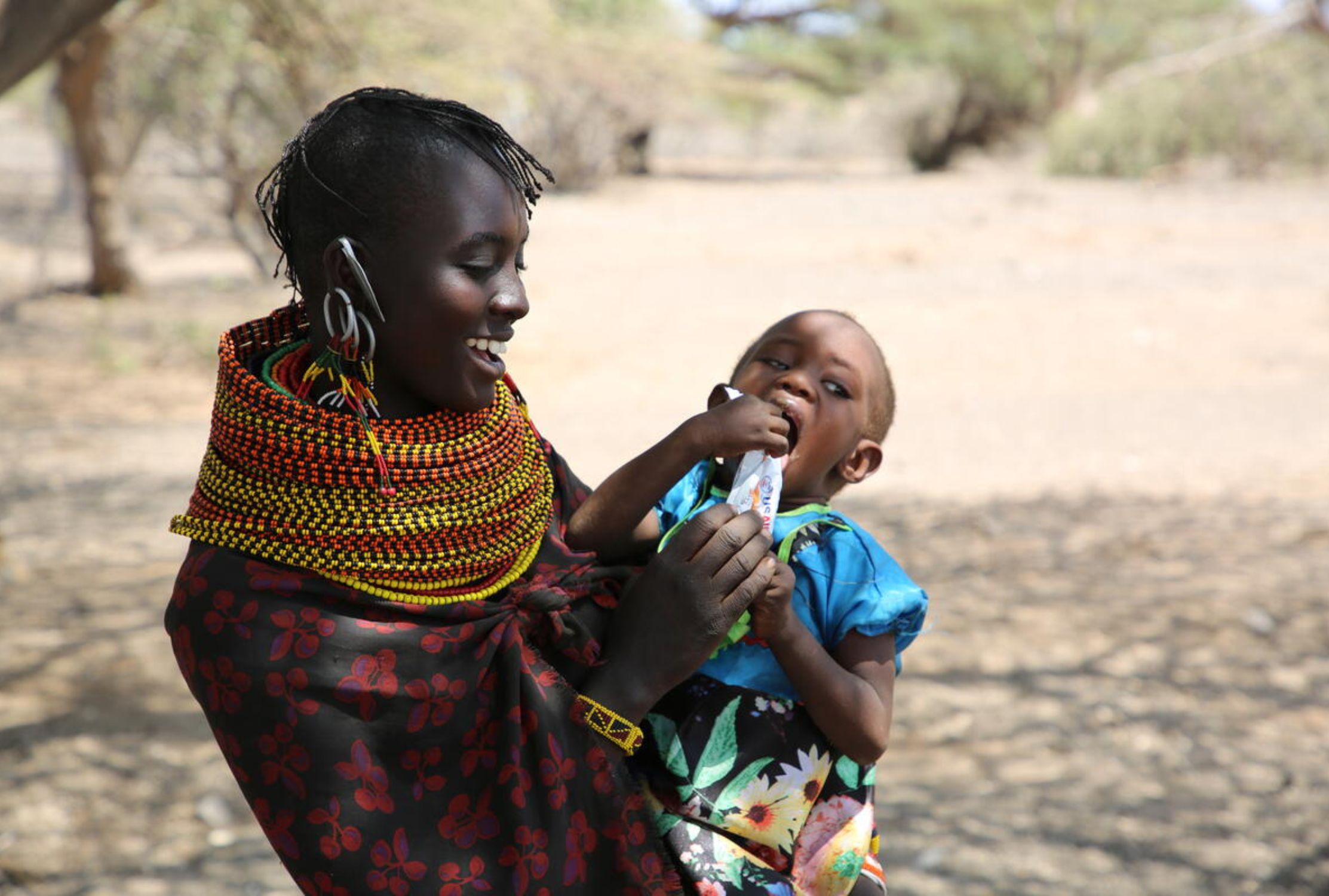 Kenyan mother holds child who is eating nutritious food aid