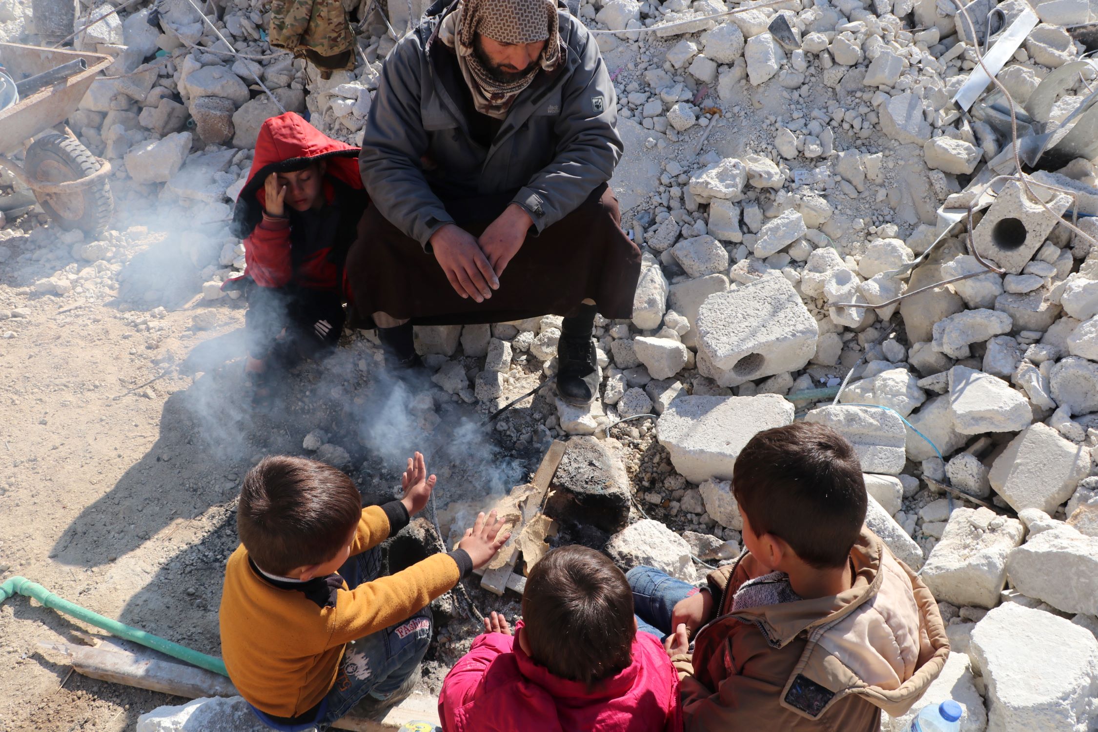 Man and children keeping warm around an outside fire amid earthquake rubble in Syria
