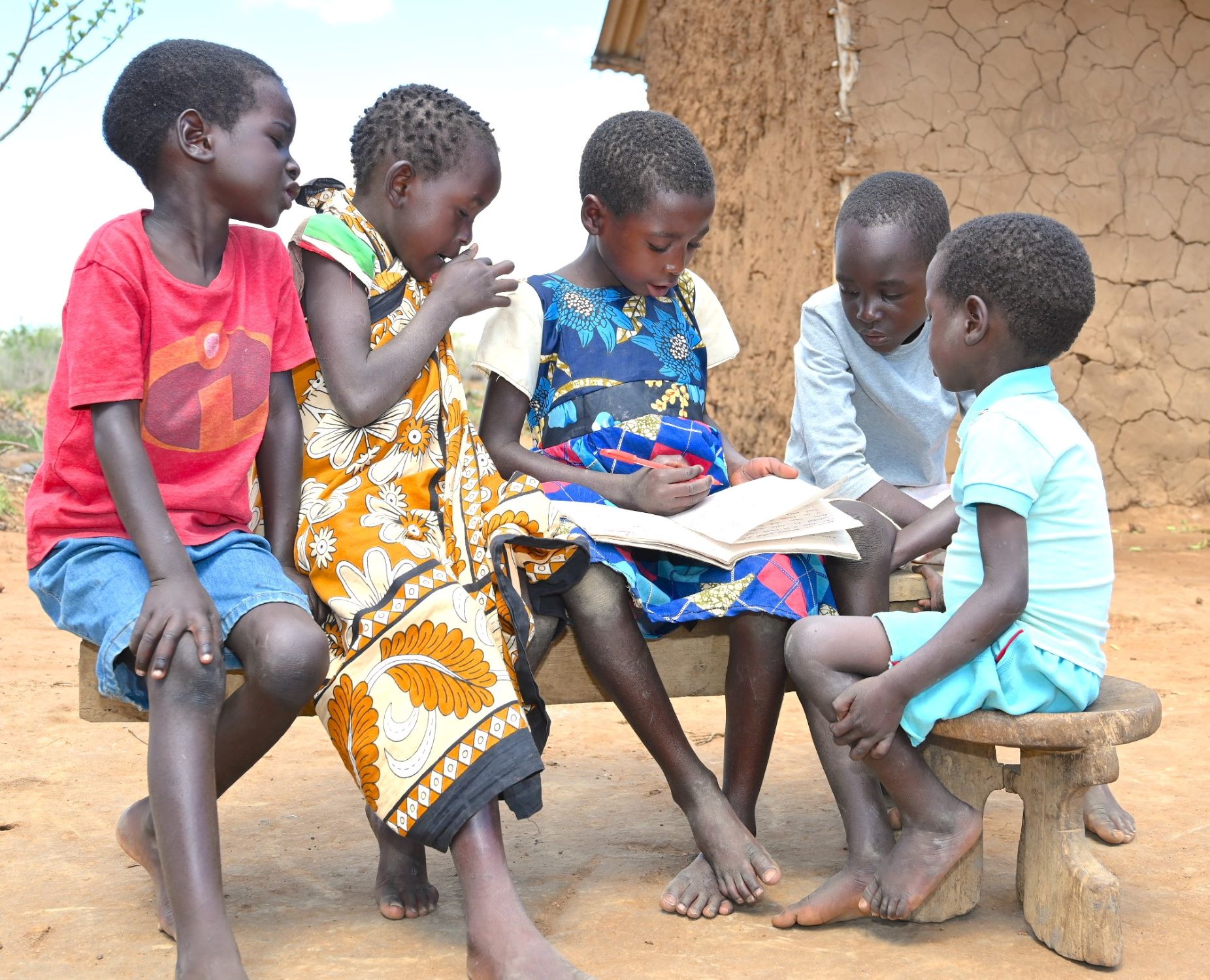 Kenyan children affected by drought reading a book outside their home