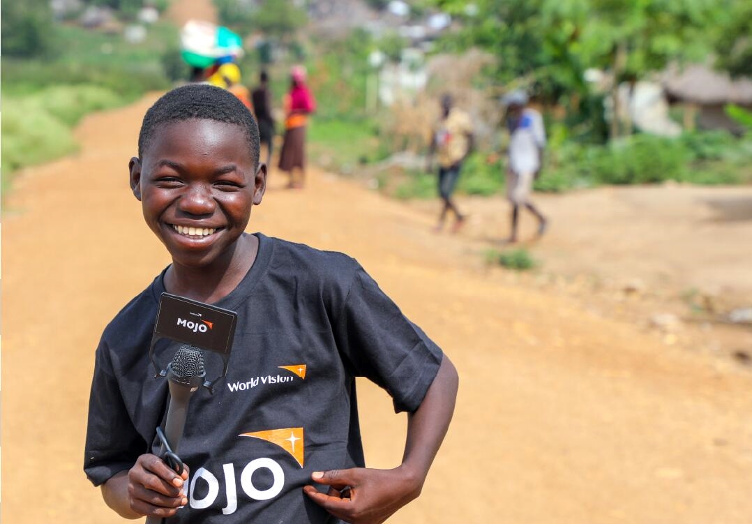 Job, then 16, an aspiring journalist in Uganda, holds standing a microphone.
