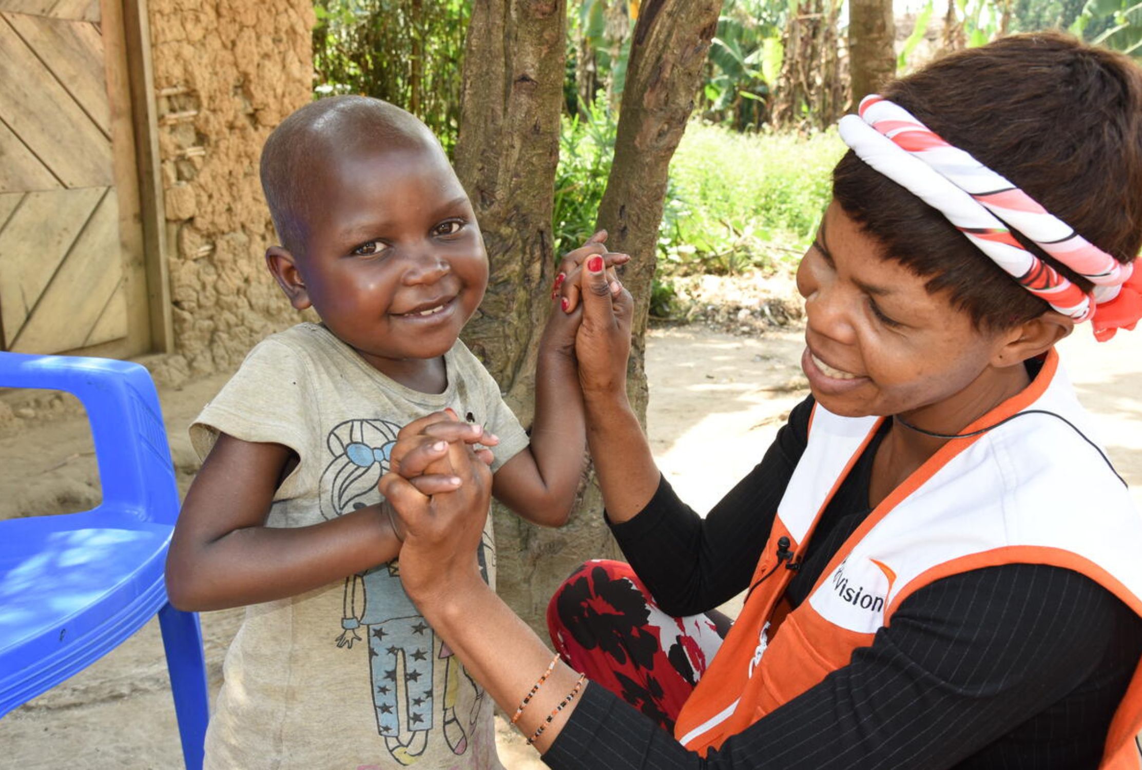 Young girl from DRC smiling at the camera while holding hands with a World Vision staff member who is looking at her