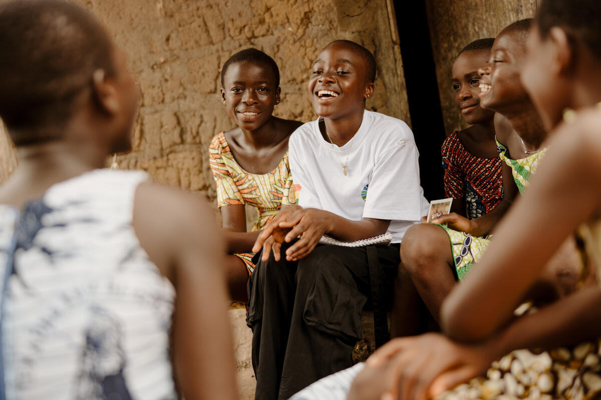 Princess sits with a group of children outside a building, chatting and laughing.