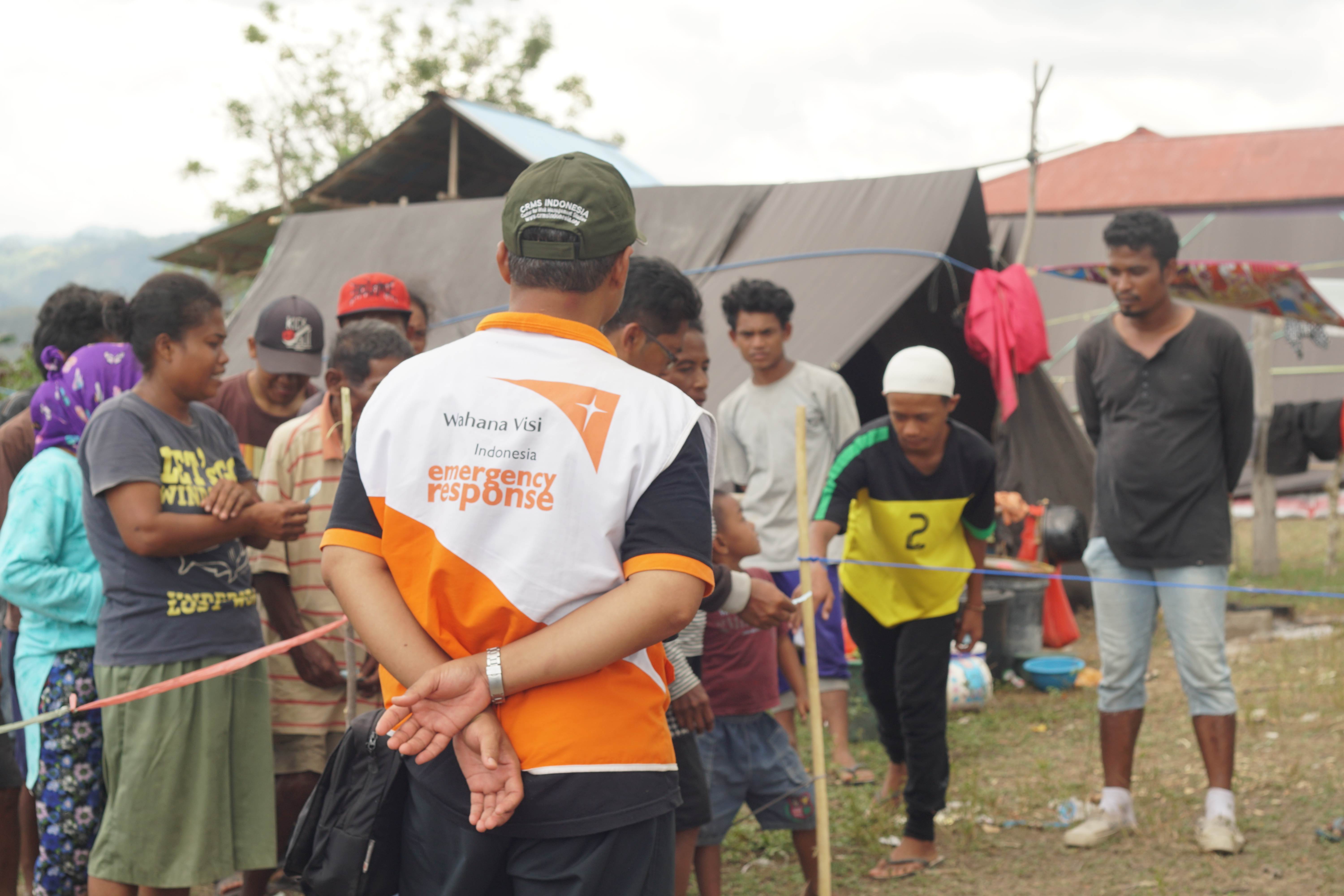 World Vision response worker in Indonesia stands looking towards a line of people standing in front of tents