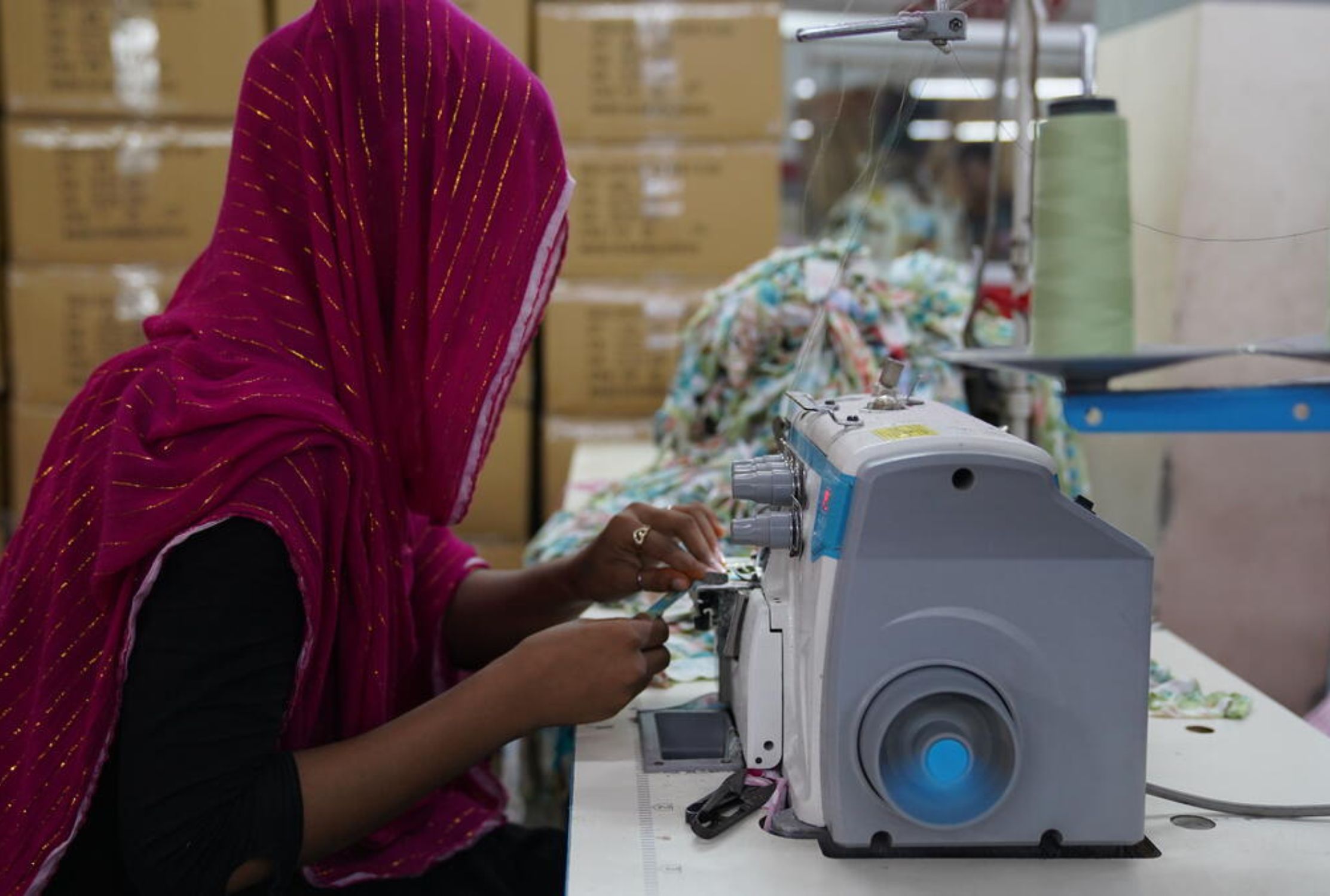 Girl in Bangladesh sews in a room, wearing a head scarf to hide her face