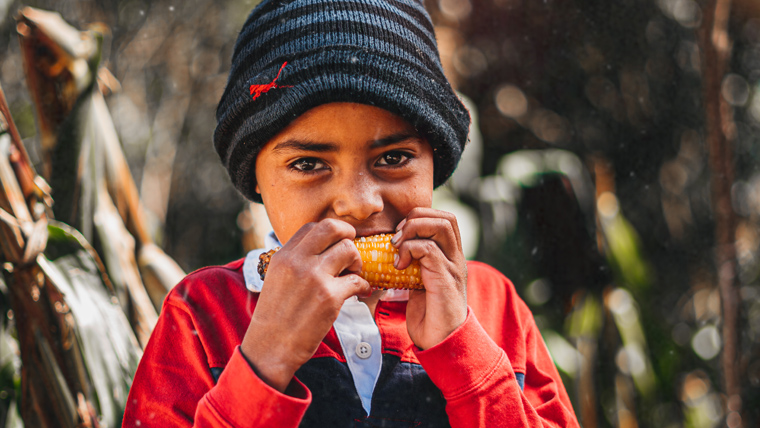 Victor in Honduras eats a freshly cooked corn cob, outside his mountain home