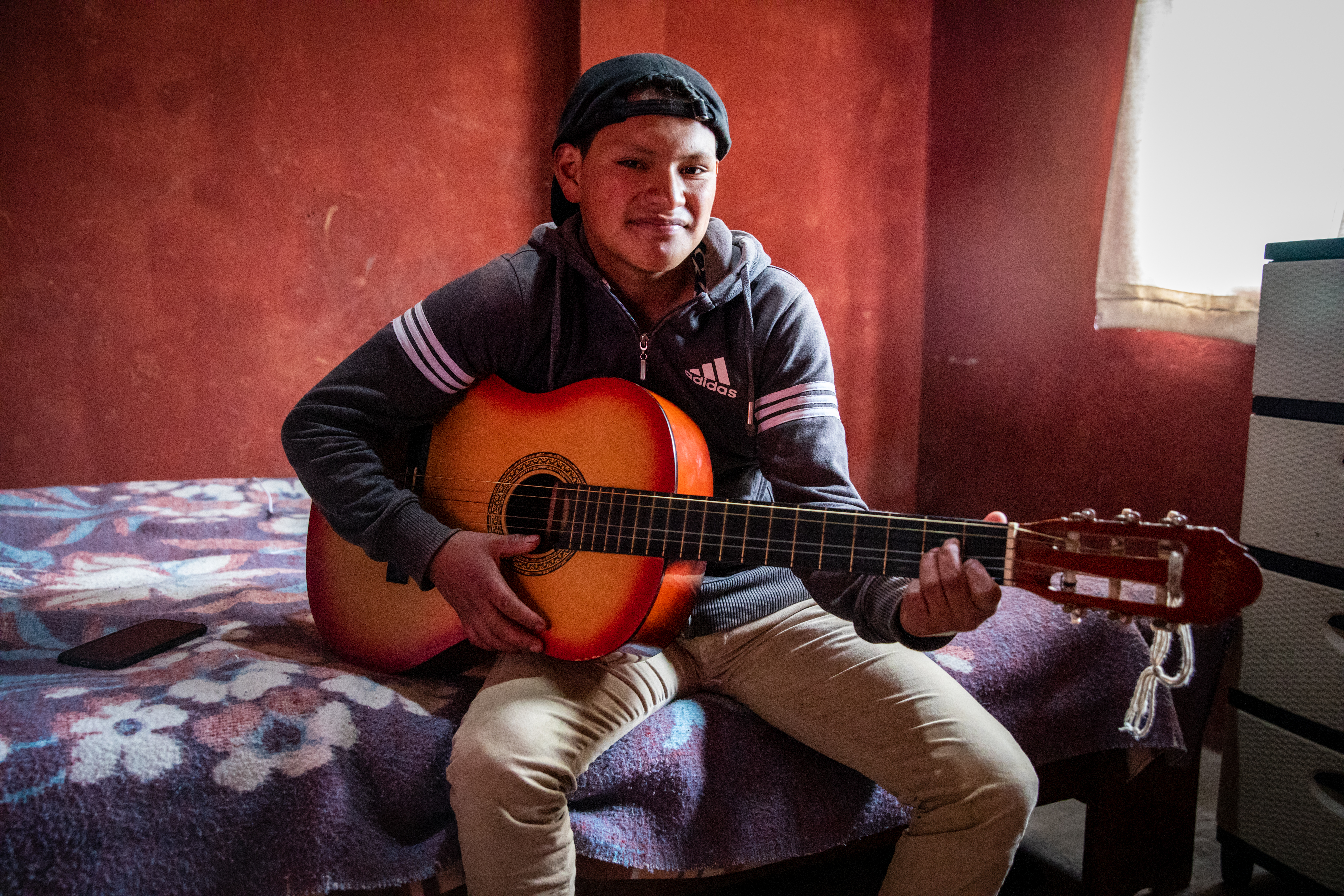 Teenage boy sits on his bed with his guitar, in Ecuador