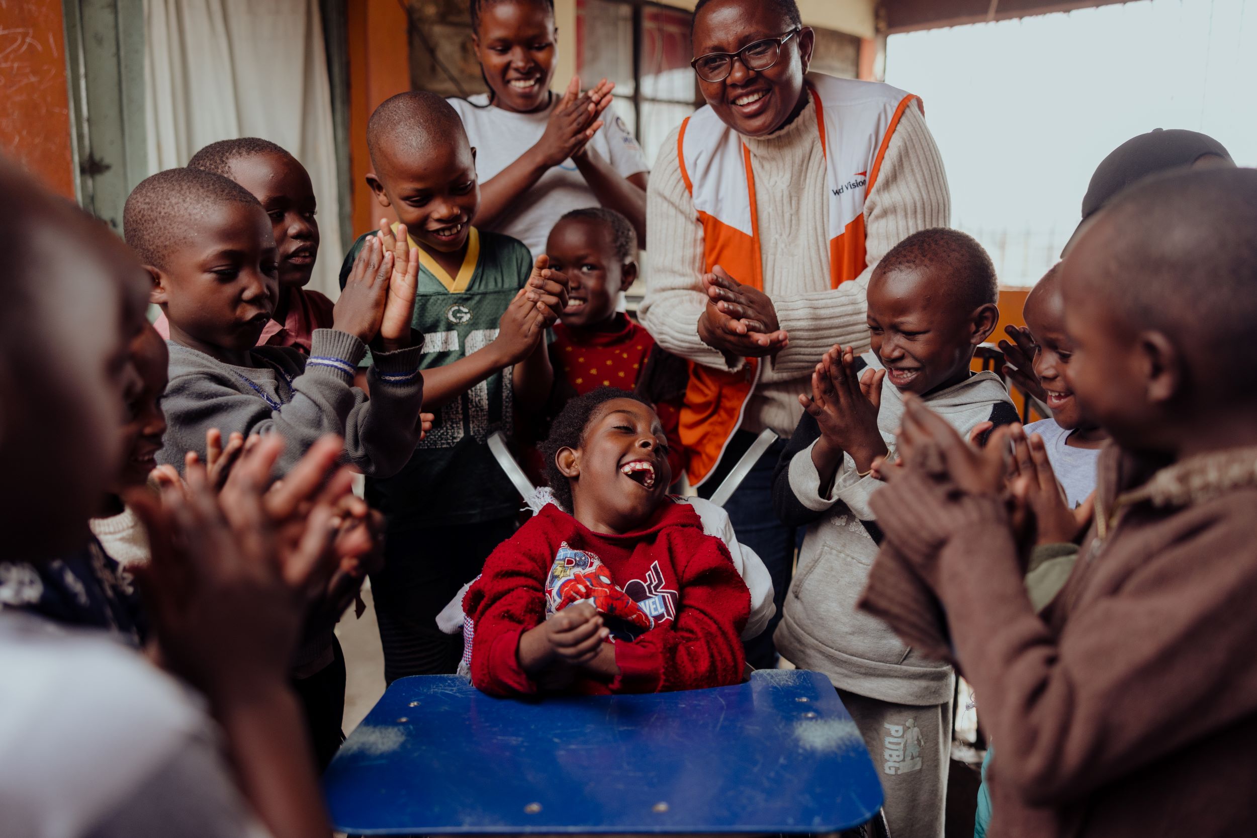 A young girl smiles in her wheelchair, surrounded by children from her community