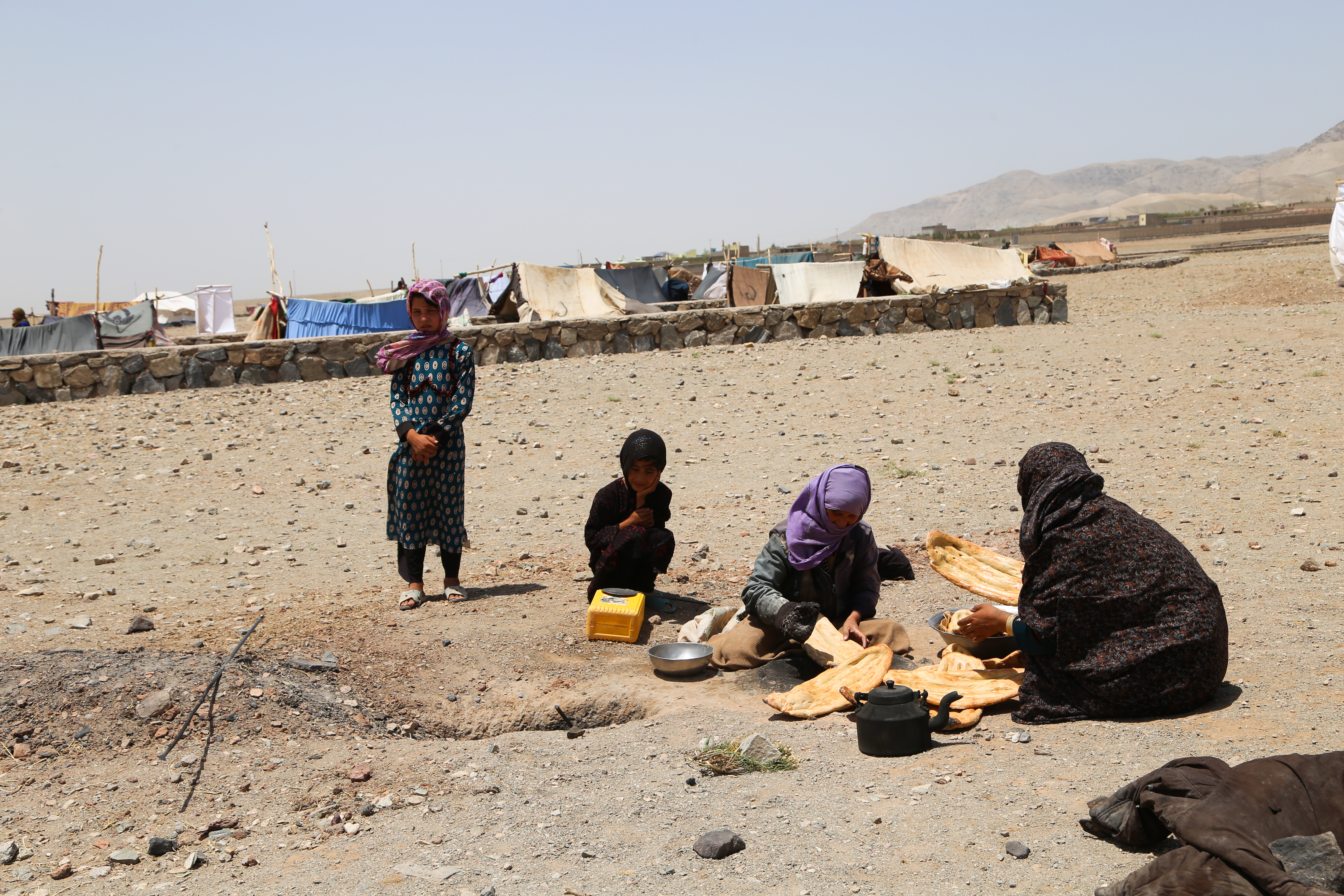 An Afghan family of four sit on the ground outside together and share food