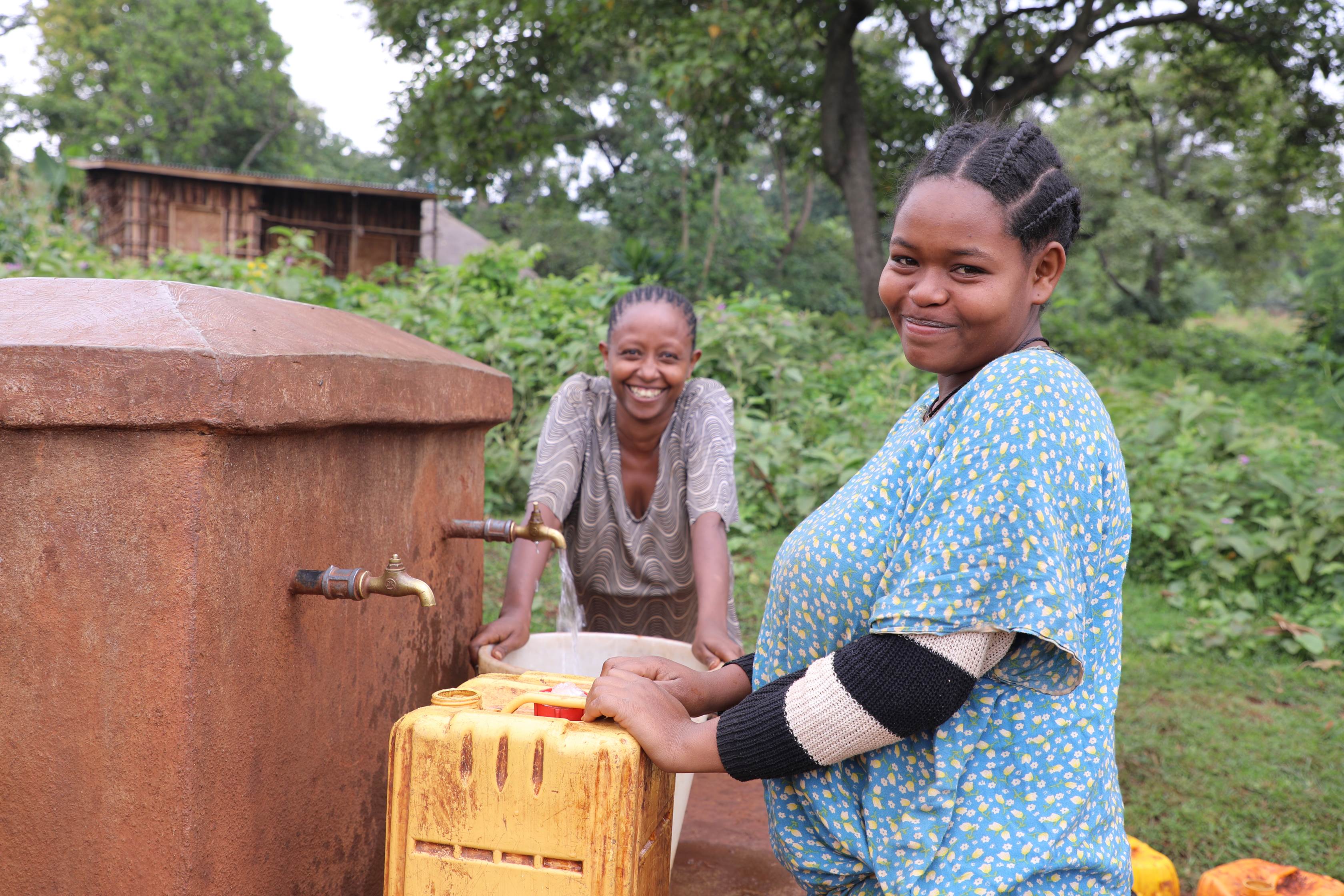 Teenage girl from Ethiopia carrying a tub of water on her back and smiling at the camera