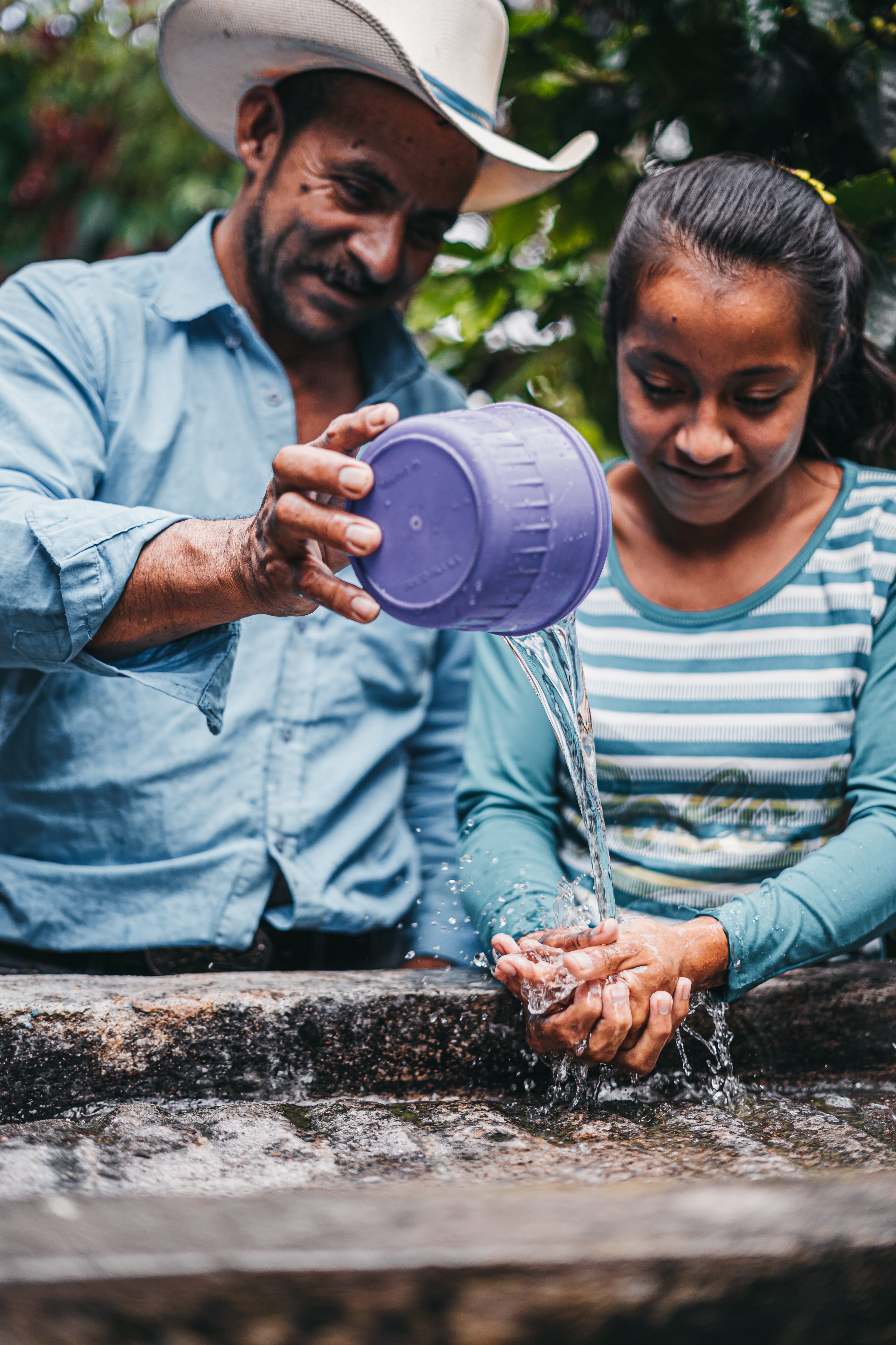 Teenage girl washing her hands and smiling, while her happy father pours the clean water for her.