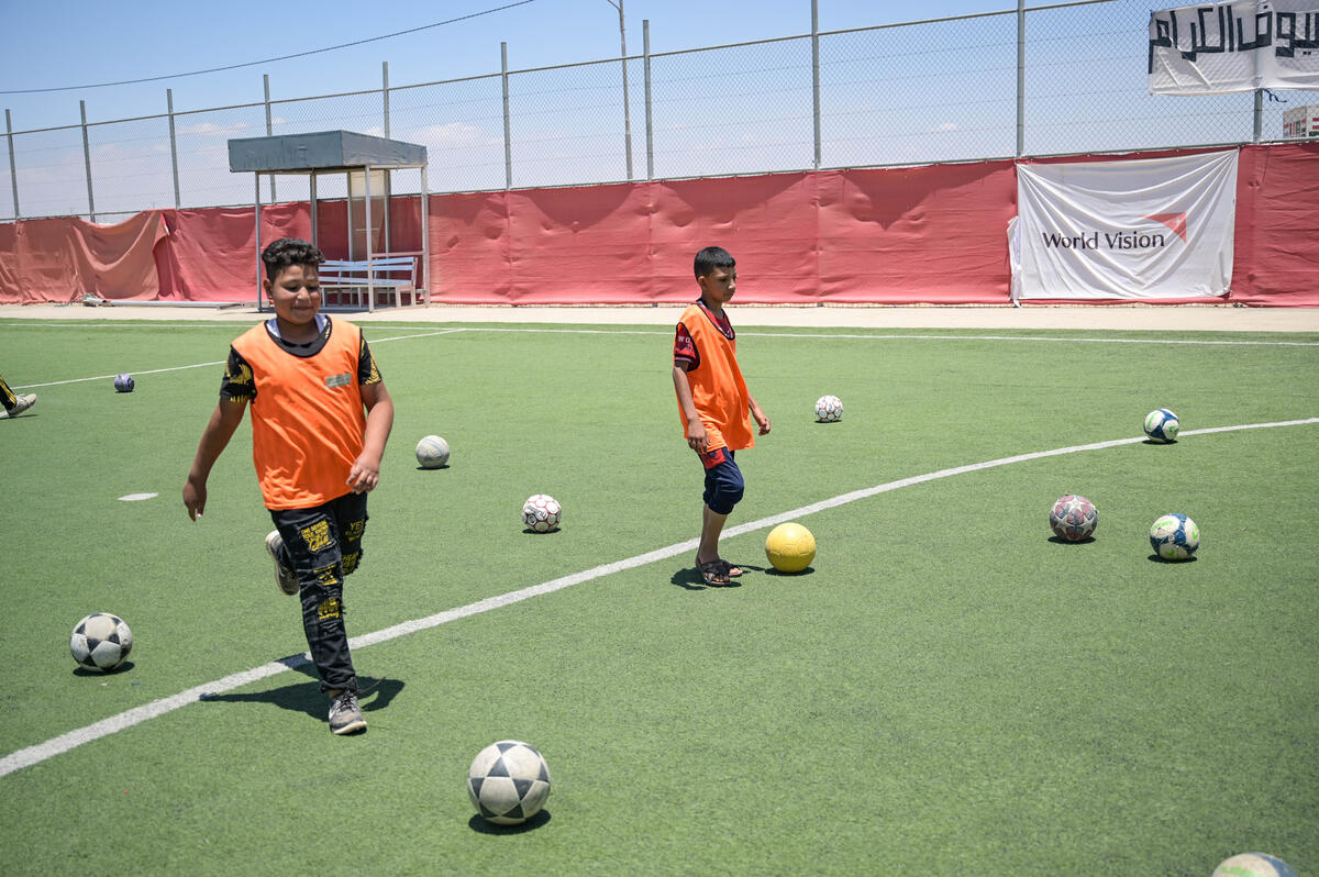 Two young balls on a sports pitch. Balls are littered everywhere.