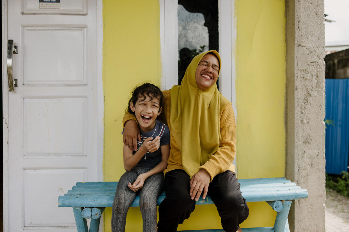 Indonesian eight-year-old girl and her mother sat on a bench laughing and smiling