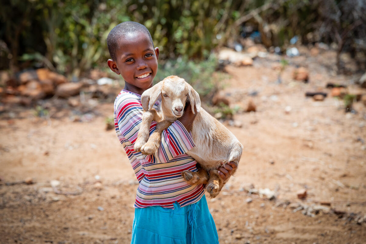 Child from Zimbabwe standing outside holding a goat and smiling to the camera