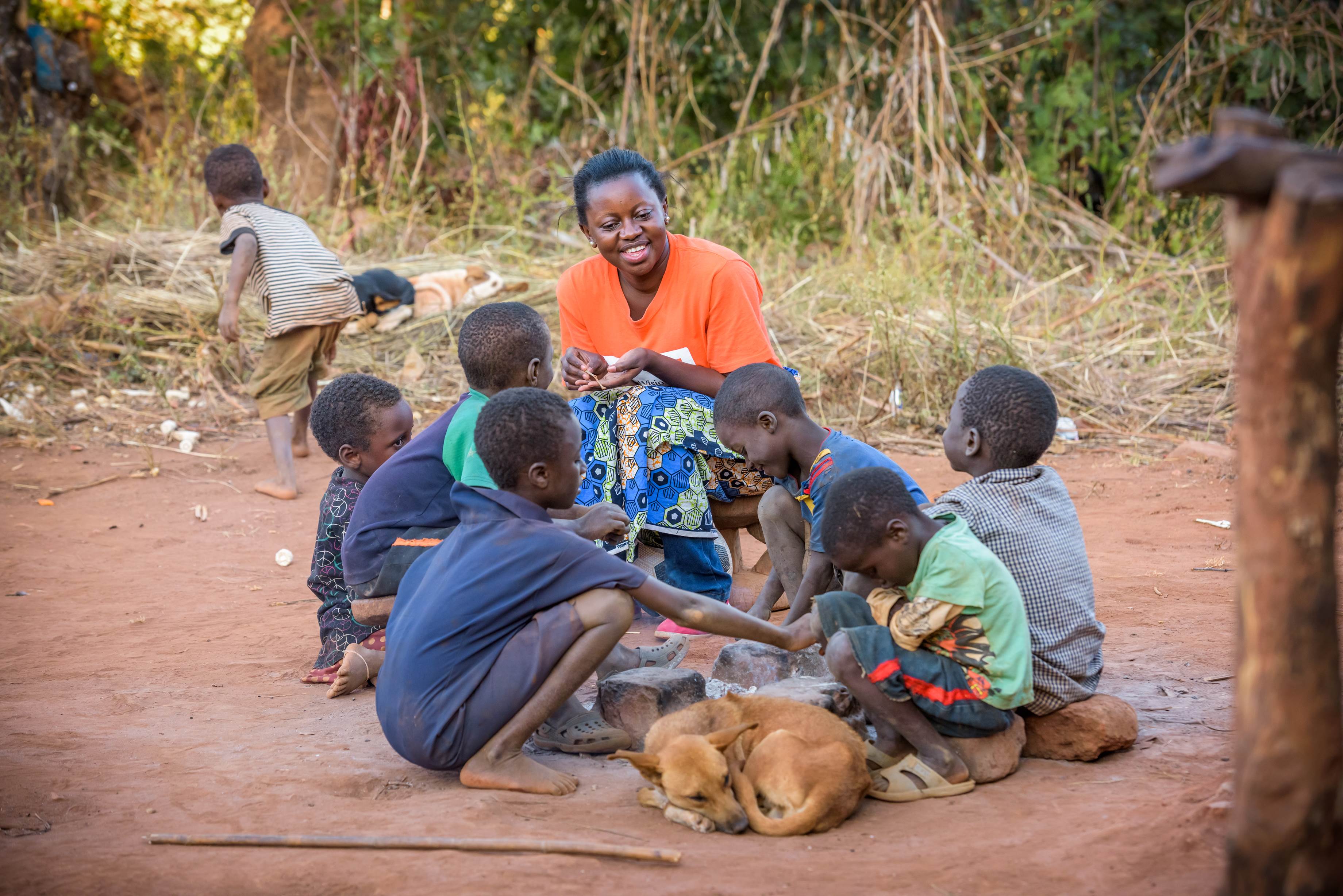 World Vision staff member sat with six children in a village in Zambia