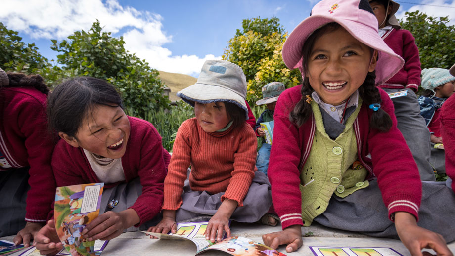 Girls in Bolivia smile broadly as they sit on the floor outside reading books