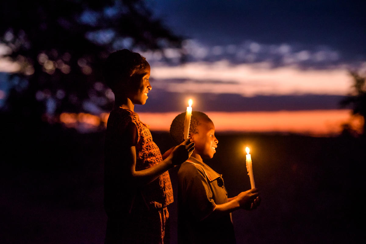Children in Zambia smile, holding candles outside against the backdrop of a sunset