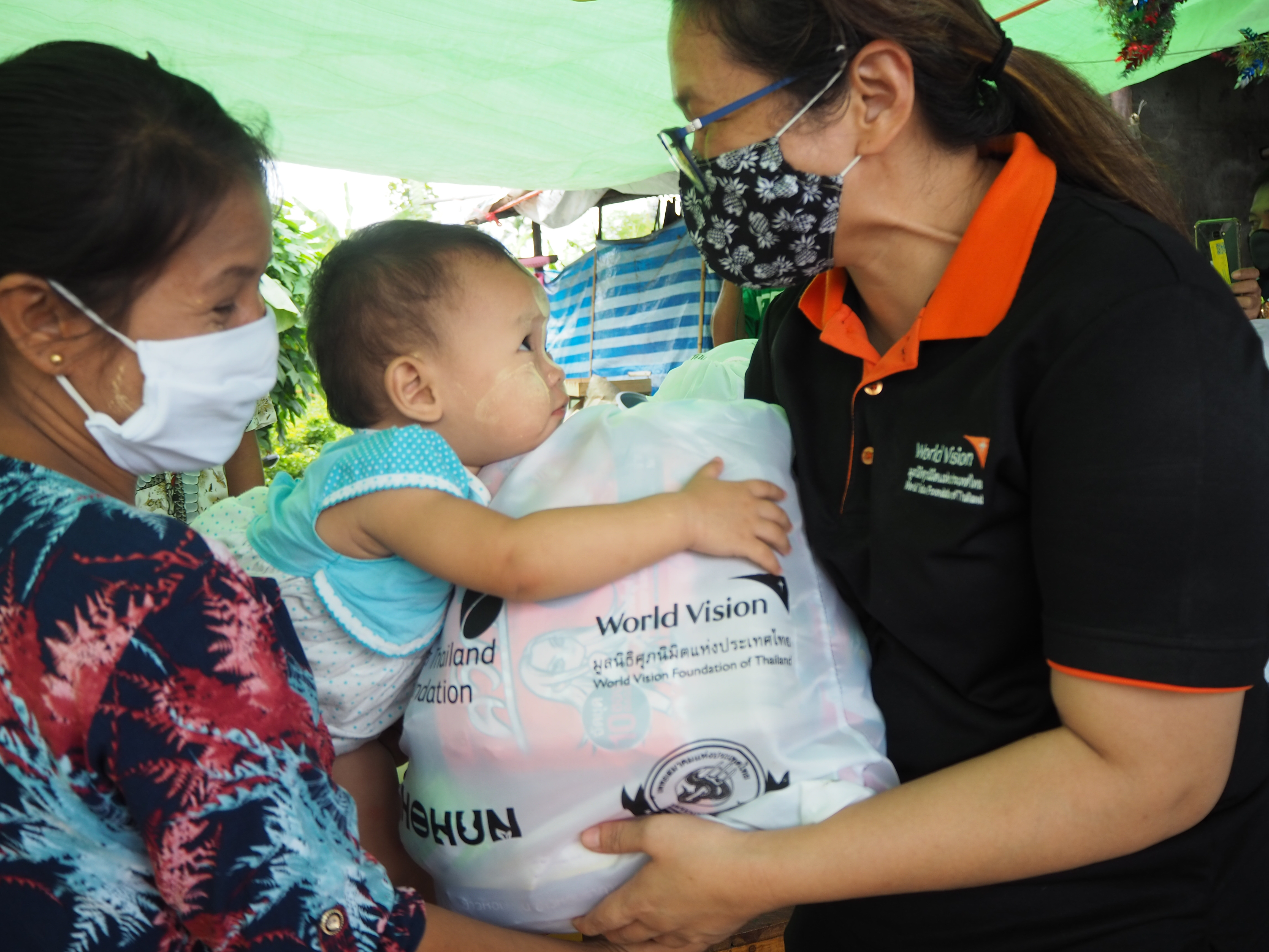 A baby leans forward in her mother's arms to grasp the food aid pack they've been given by World Vision in Myanmar.