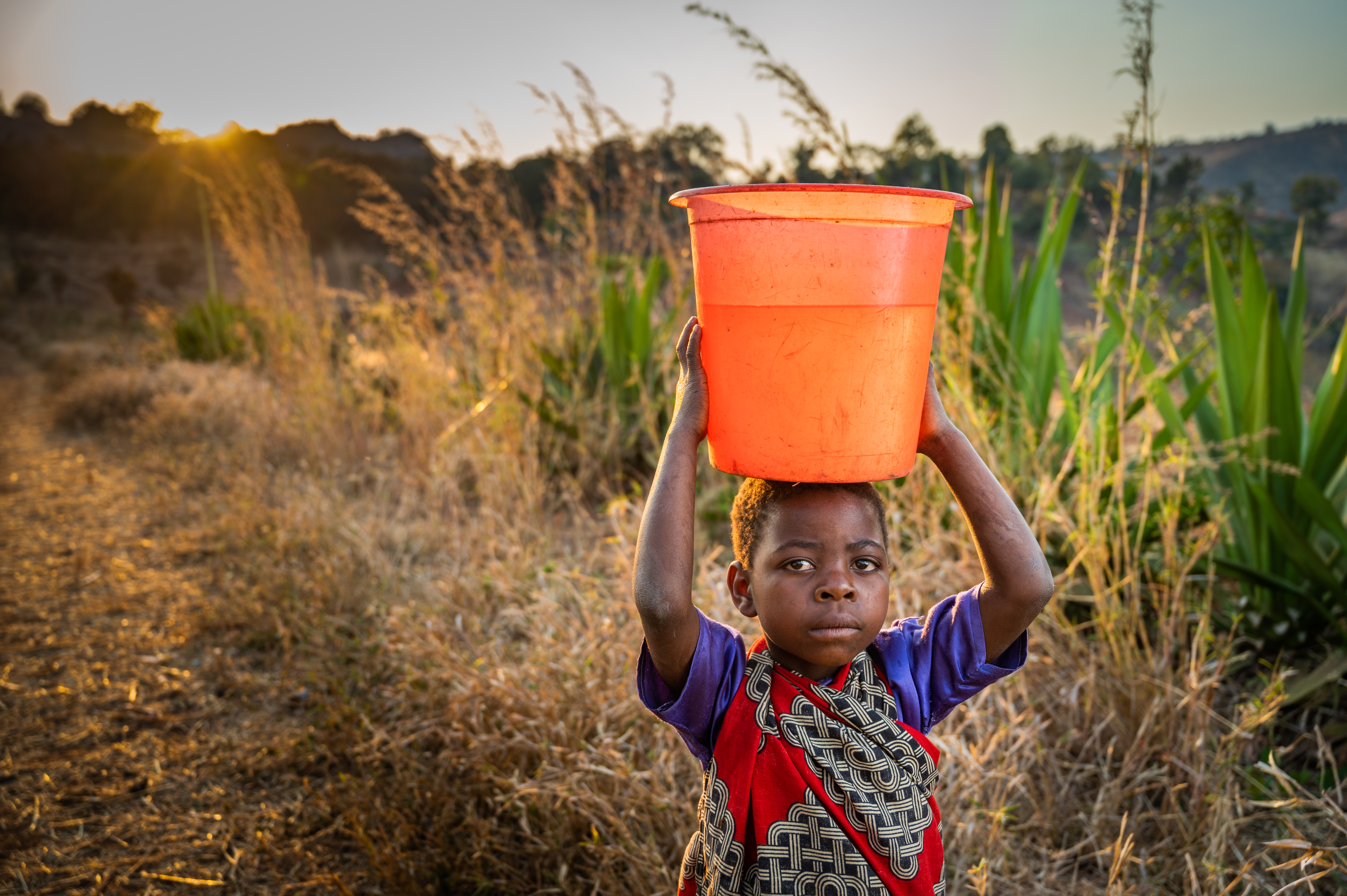 Girl from Malawi carries water in a bucket on her head