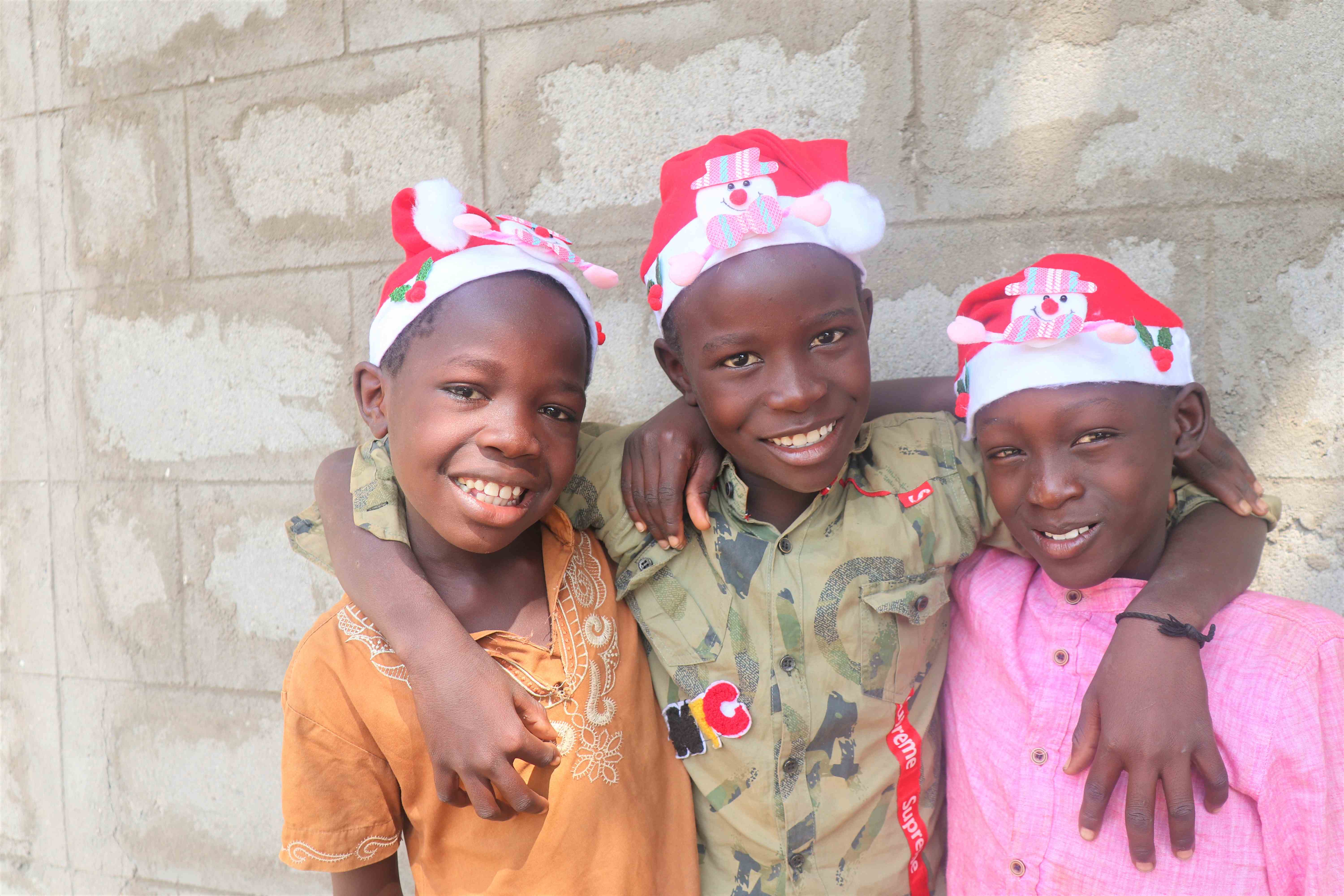 Three South Sudanese children smiling and wearing Christmas hats