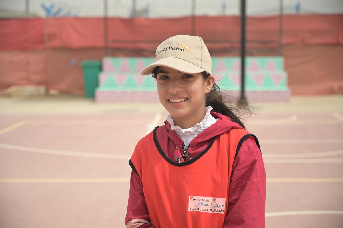 A young girl wearing a World Vision Hat smiles at the camera