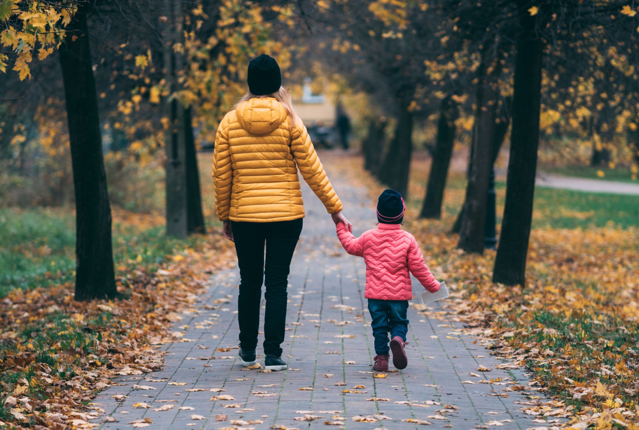 Mother and child walking between trees with autumnal orange leaves