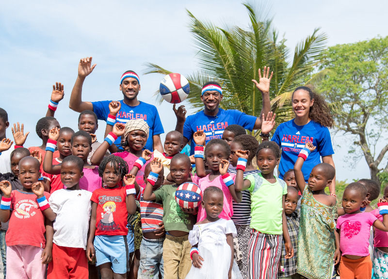 Members of the Harlem Globetrotters smile and wave their hands in the air as they pose with a group of children