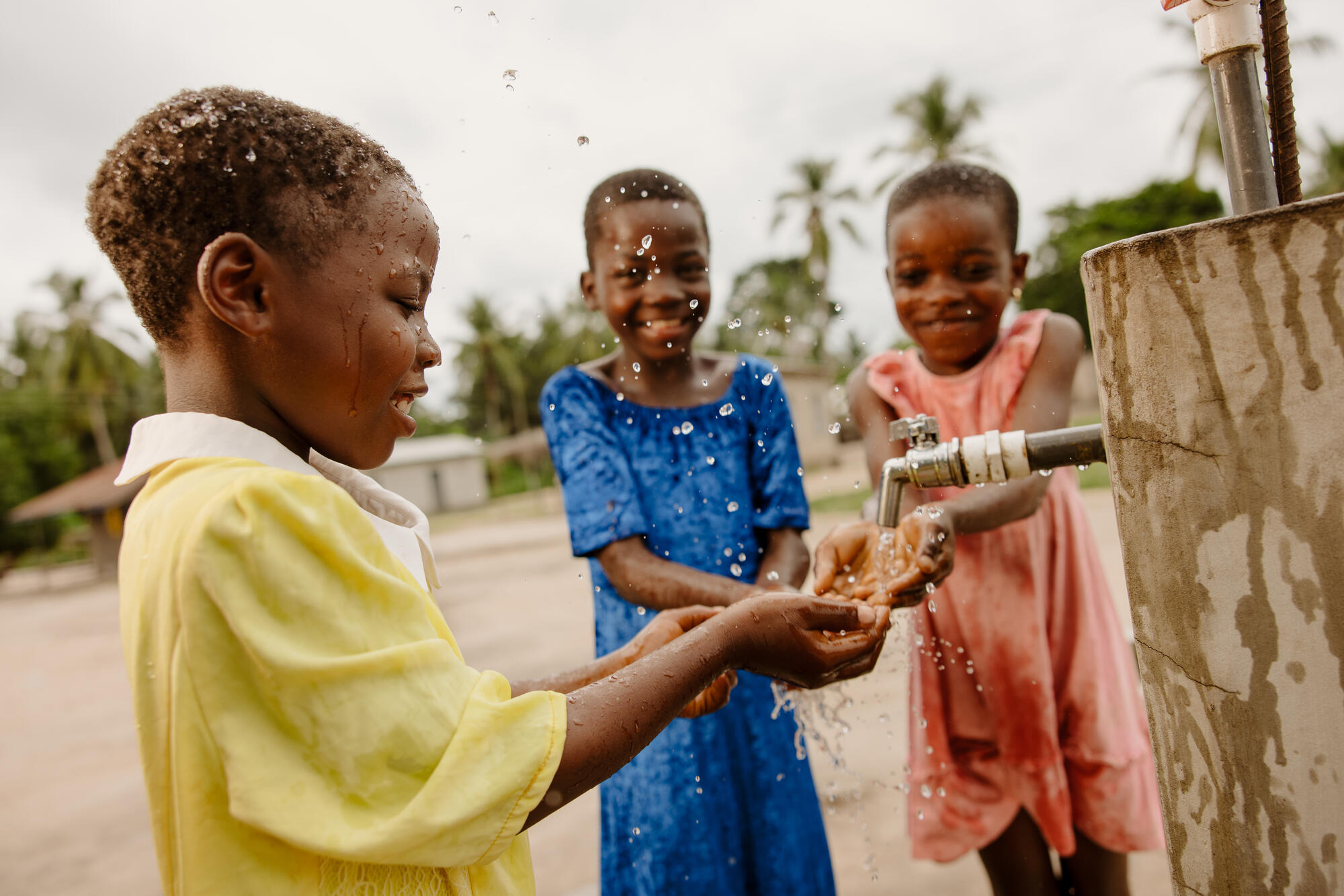 Children in Ghana laugh as they wash their hands beneath a tap