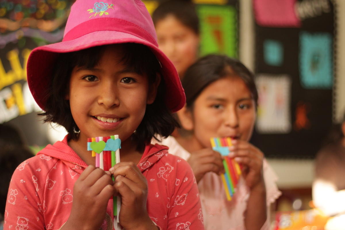 Young Bolivian girl wearing pink hat holds homemade panpipes in a classroom