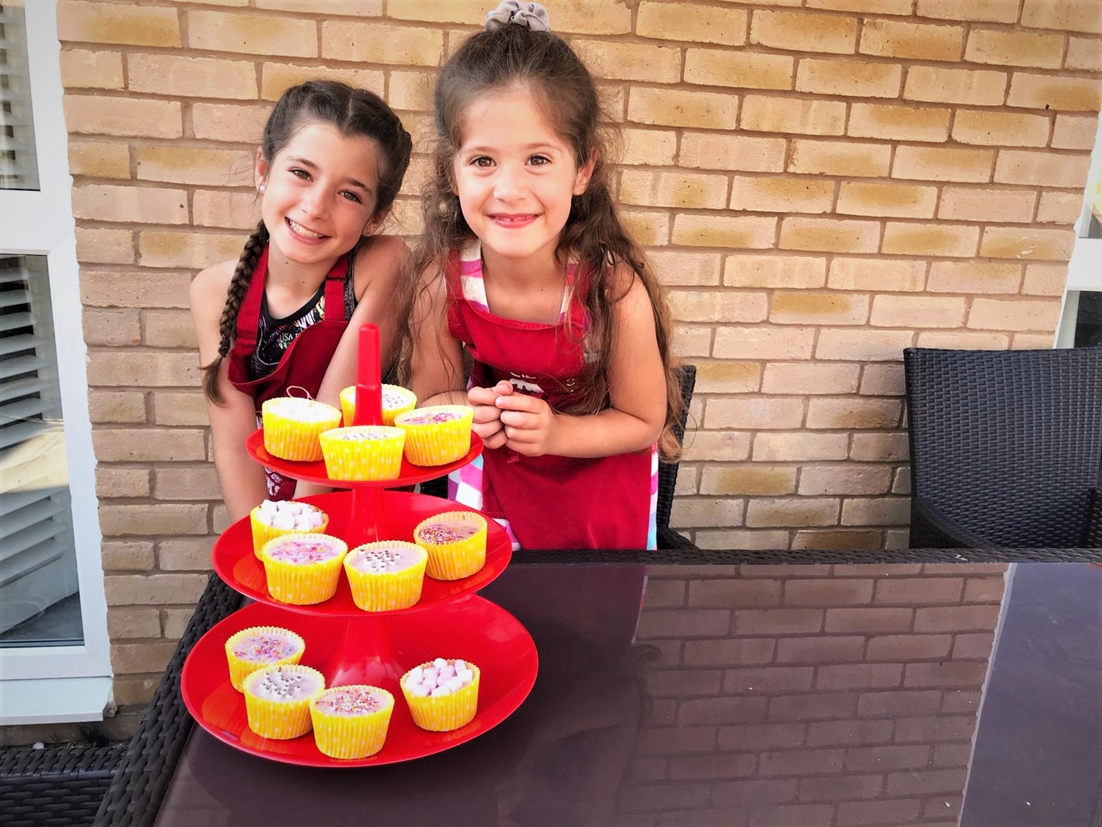 Two children smiling to the camera behind a tower of cupcakes
