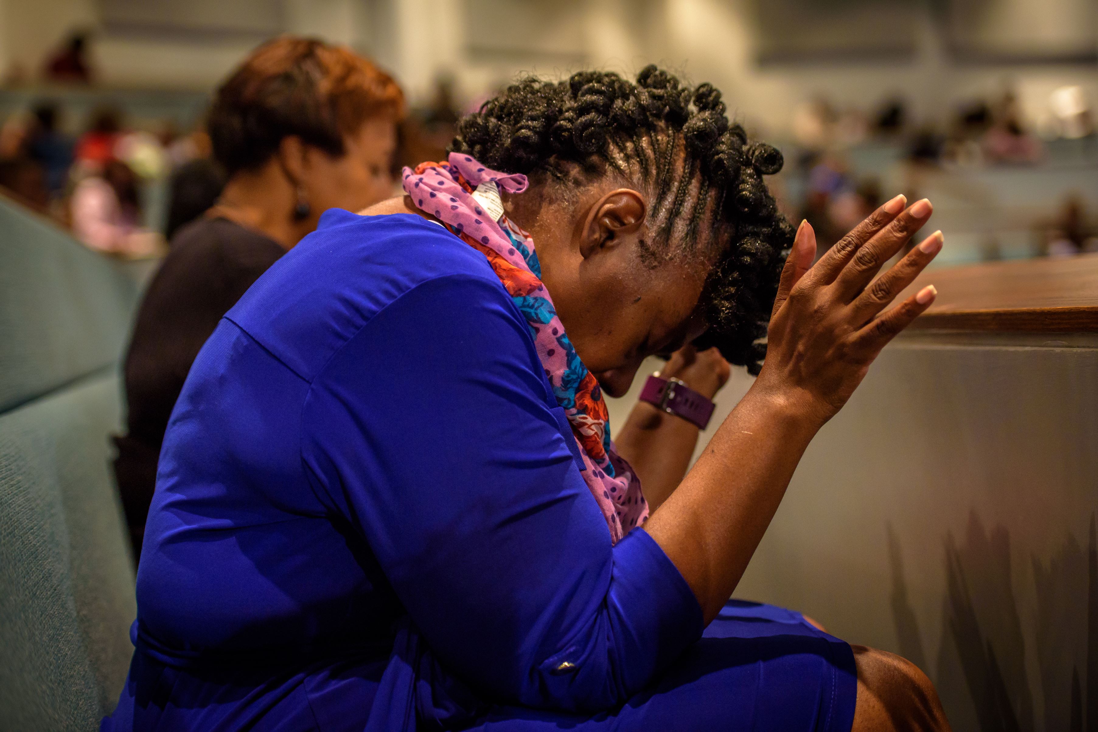 Woman sits in a pew, head bent over her hands in prayer in the USA