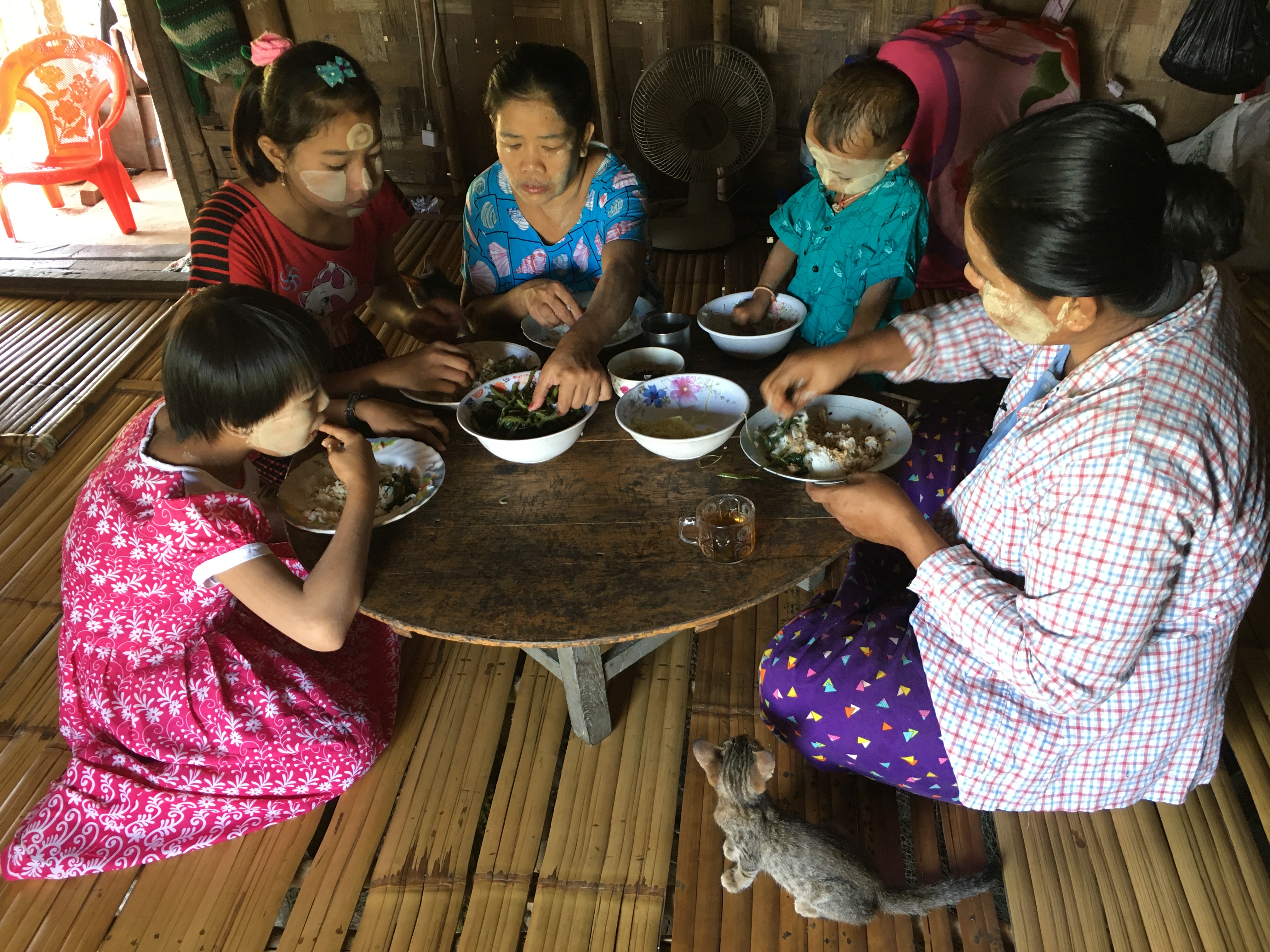 Woman from Myanmar and her 4 children sitting in a circle on the floor and eating with their hands from a round table.