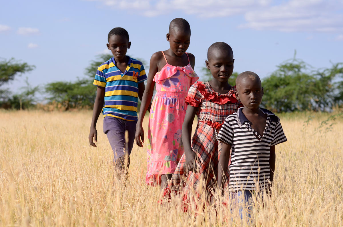 Four young children walk through withered crops in Kenya