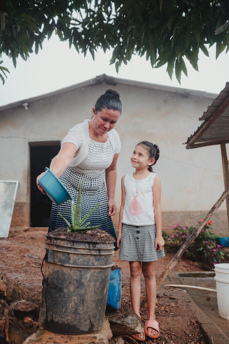 Mother and daughter stood smiling as they water some plants. 