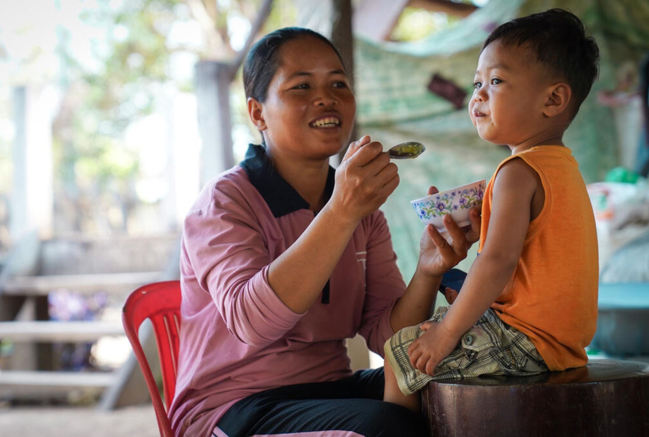 Cambodian mother feeding her son from a bowl and spoon
