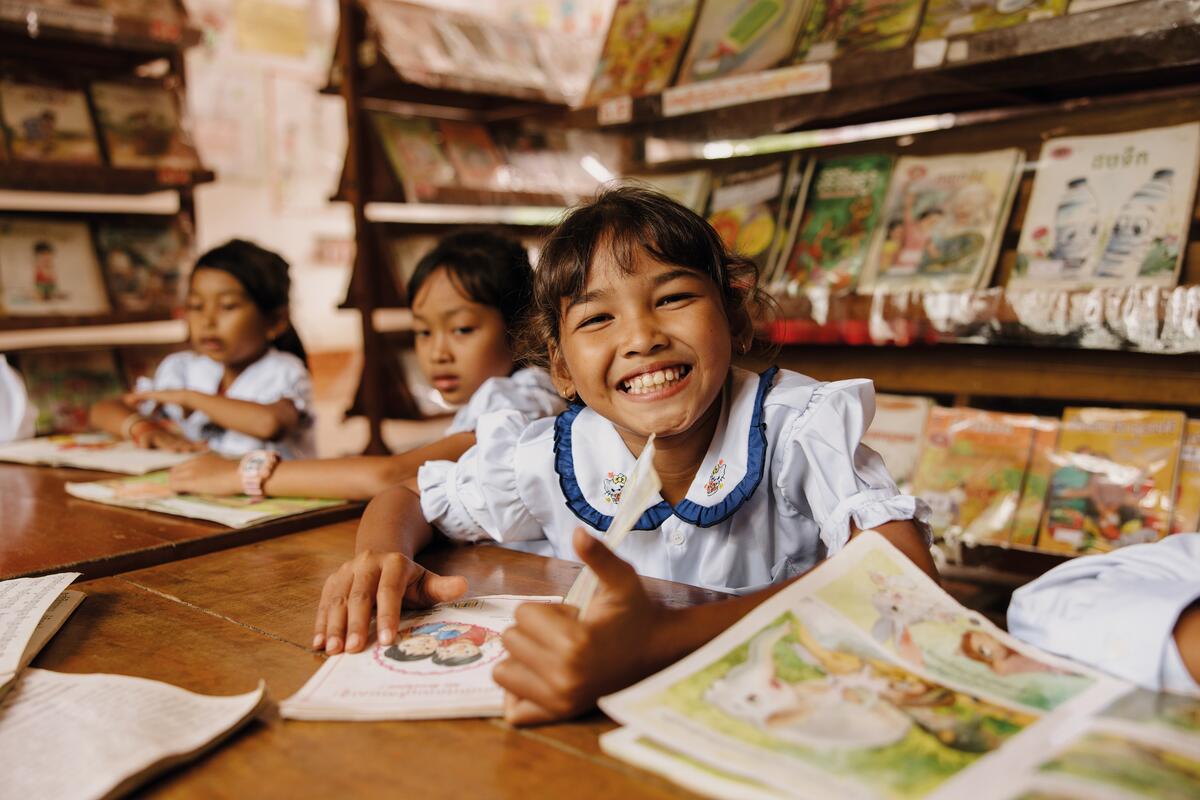 Girl in Cambodia smiles as she sits at a school desk amongst peers