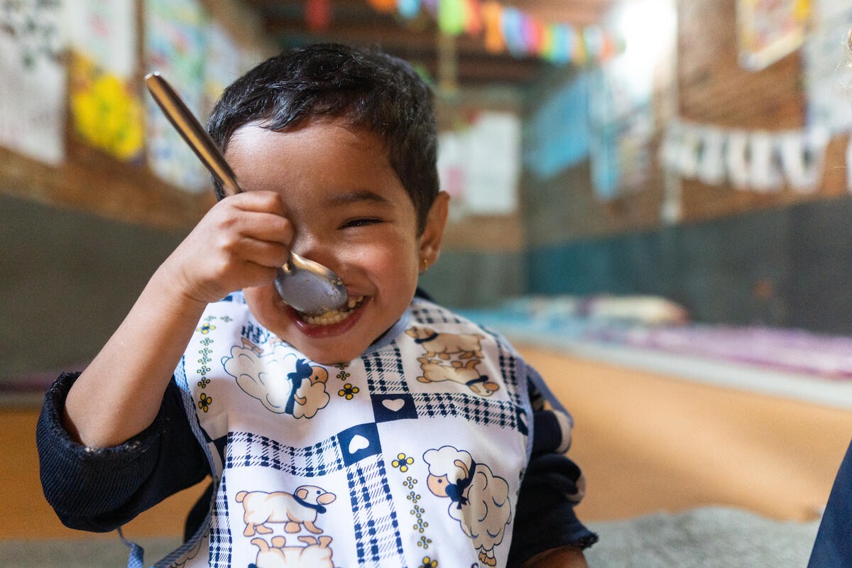 A little boy sat in room, grinning a big smile as he eats from a spoon