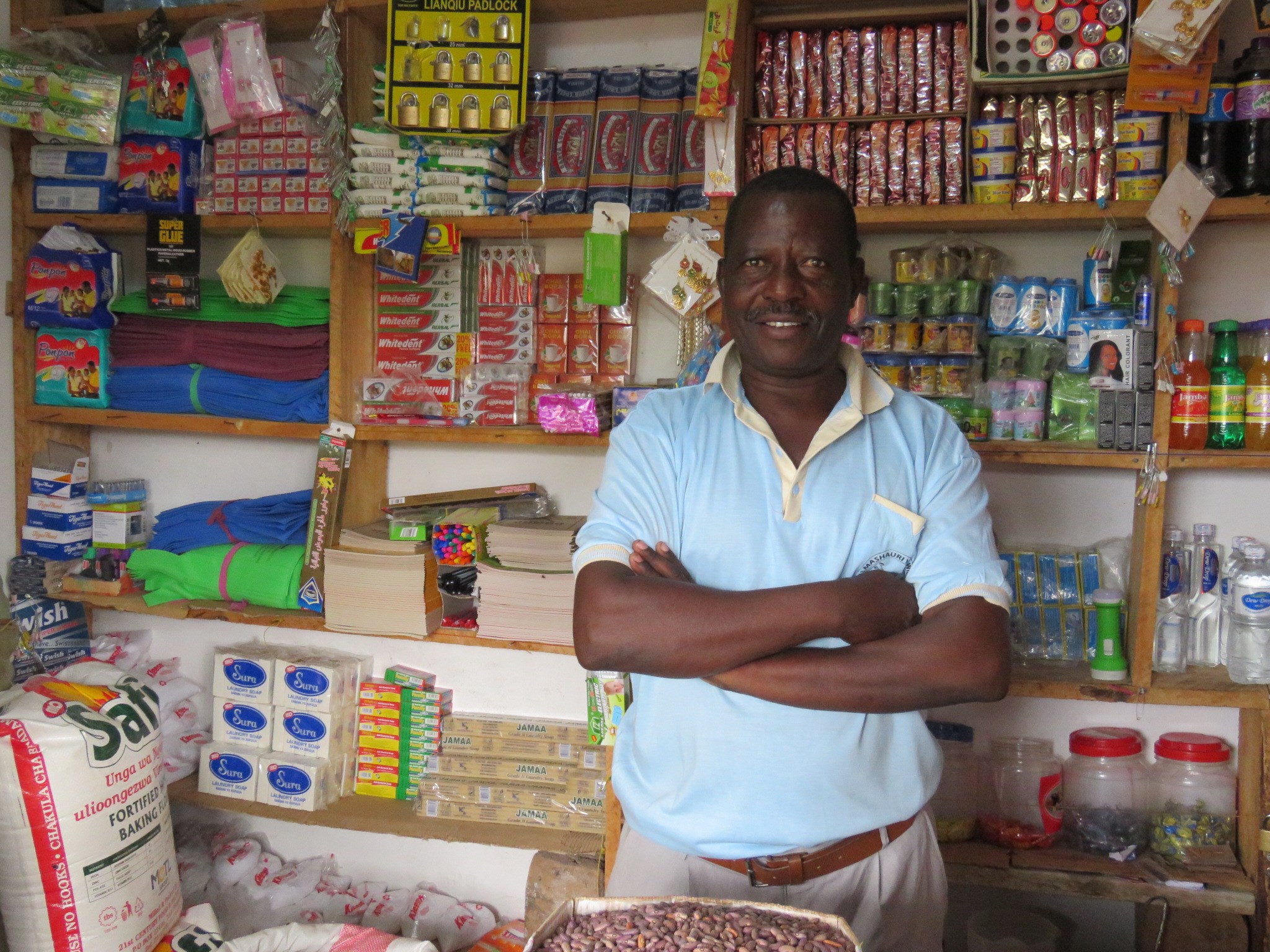 Man from Tanzania stands with his arms folded inside his show, with a wall of confectionary around him