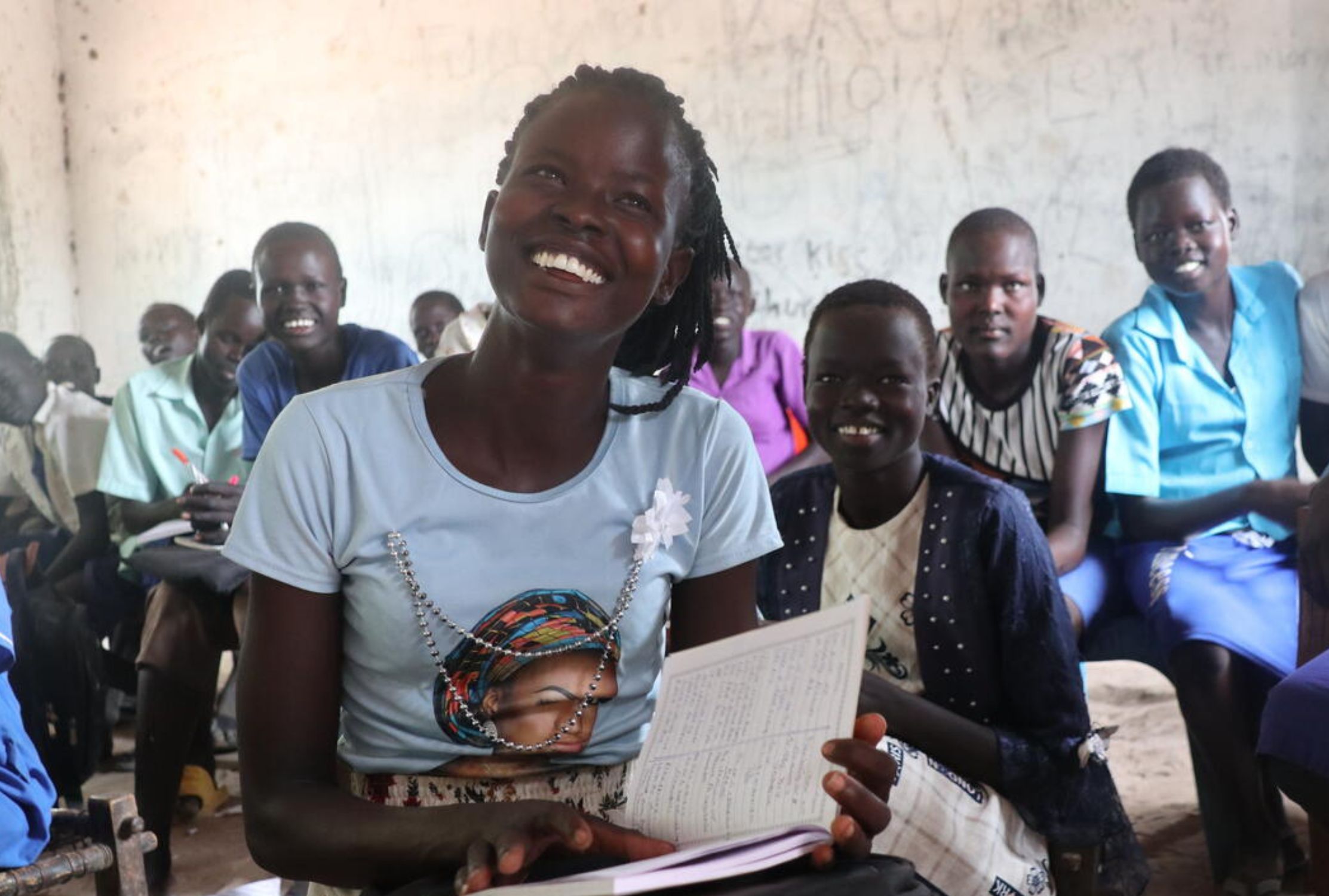 South Sudanese woman smiling with a notebook in a classroom