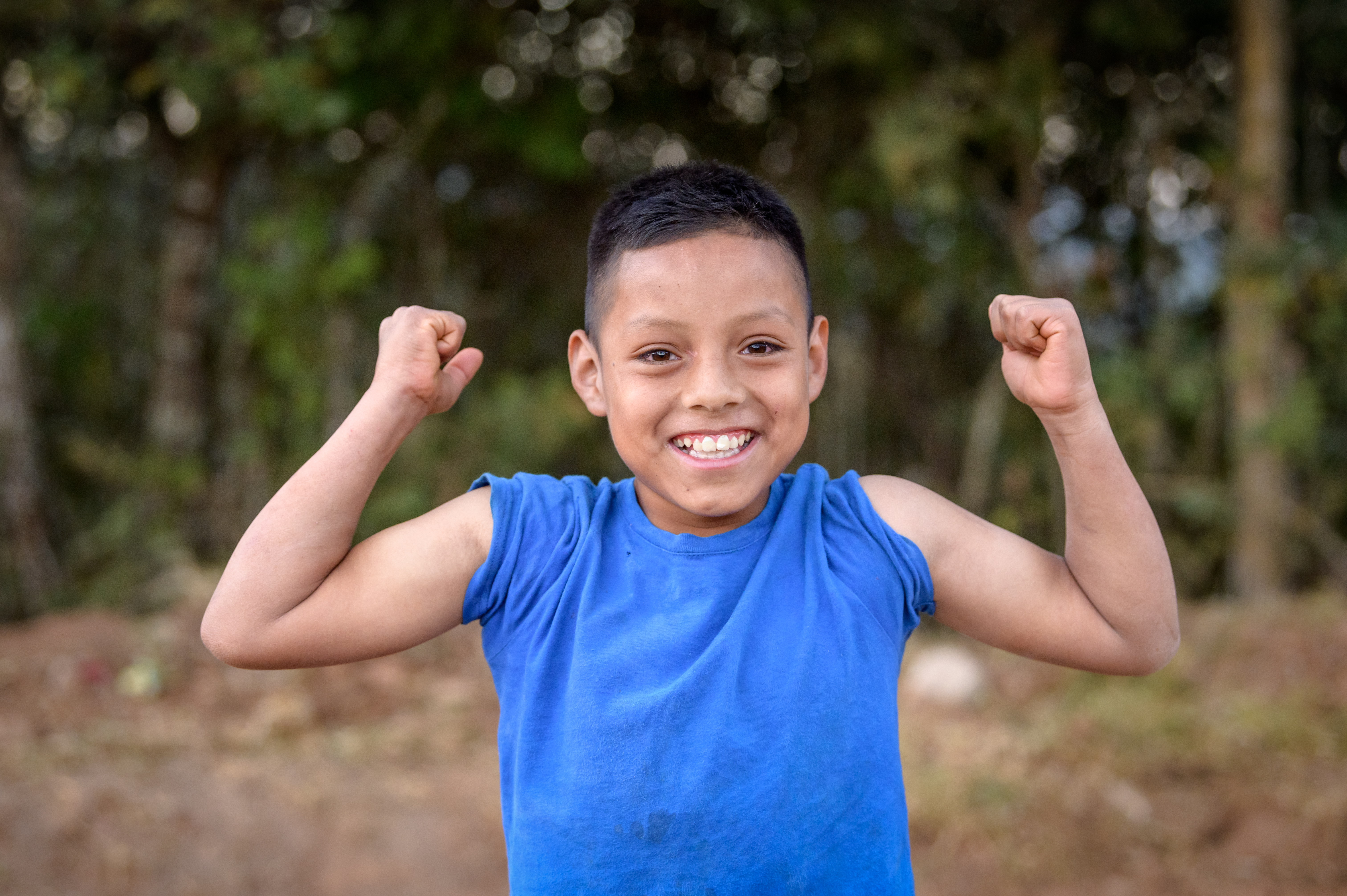 Sponsored child from Honduras grins widely as he shows off his muscles to the camera